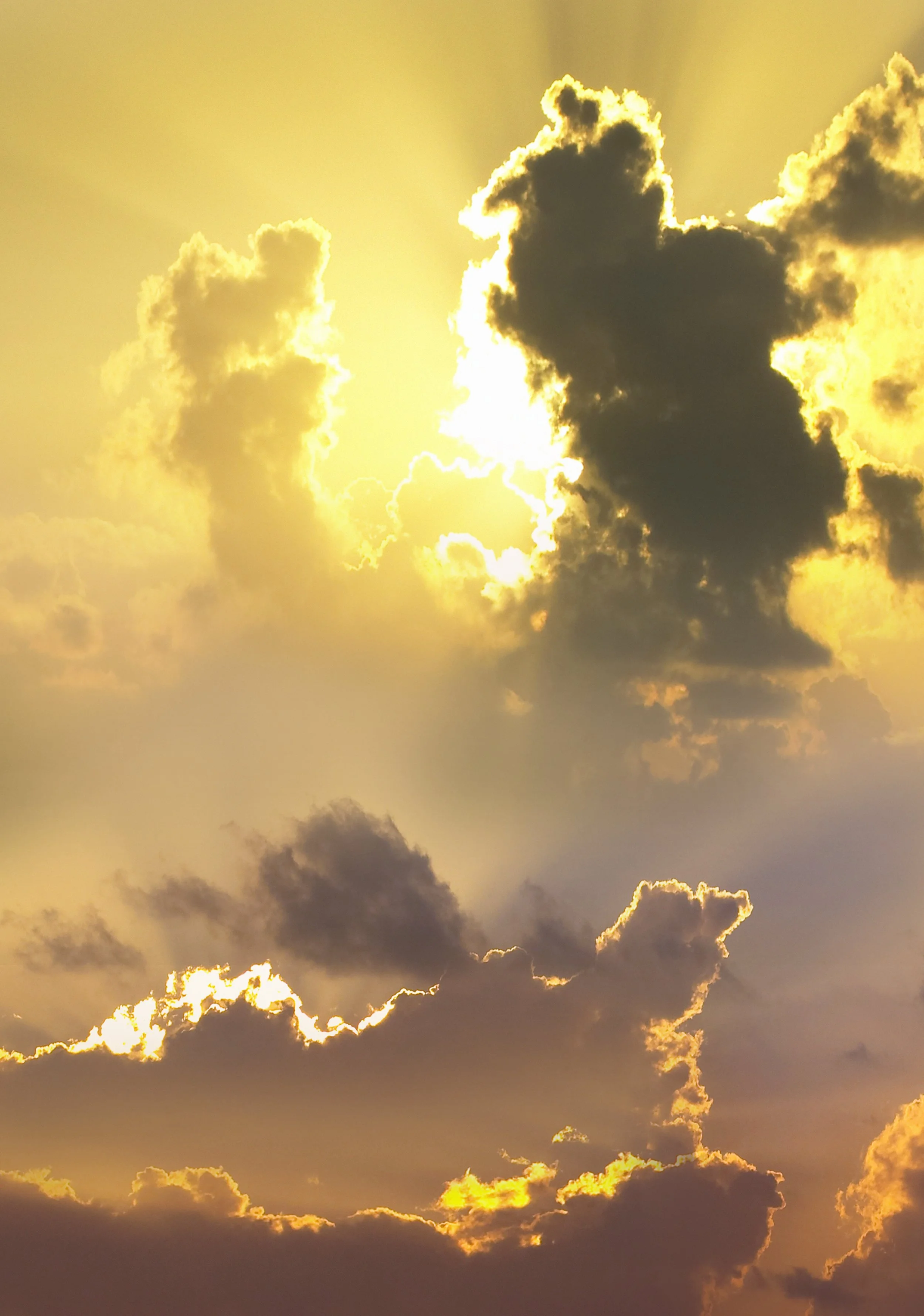 Sun shining through dark and light clouds in a golden sky.
