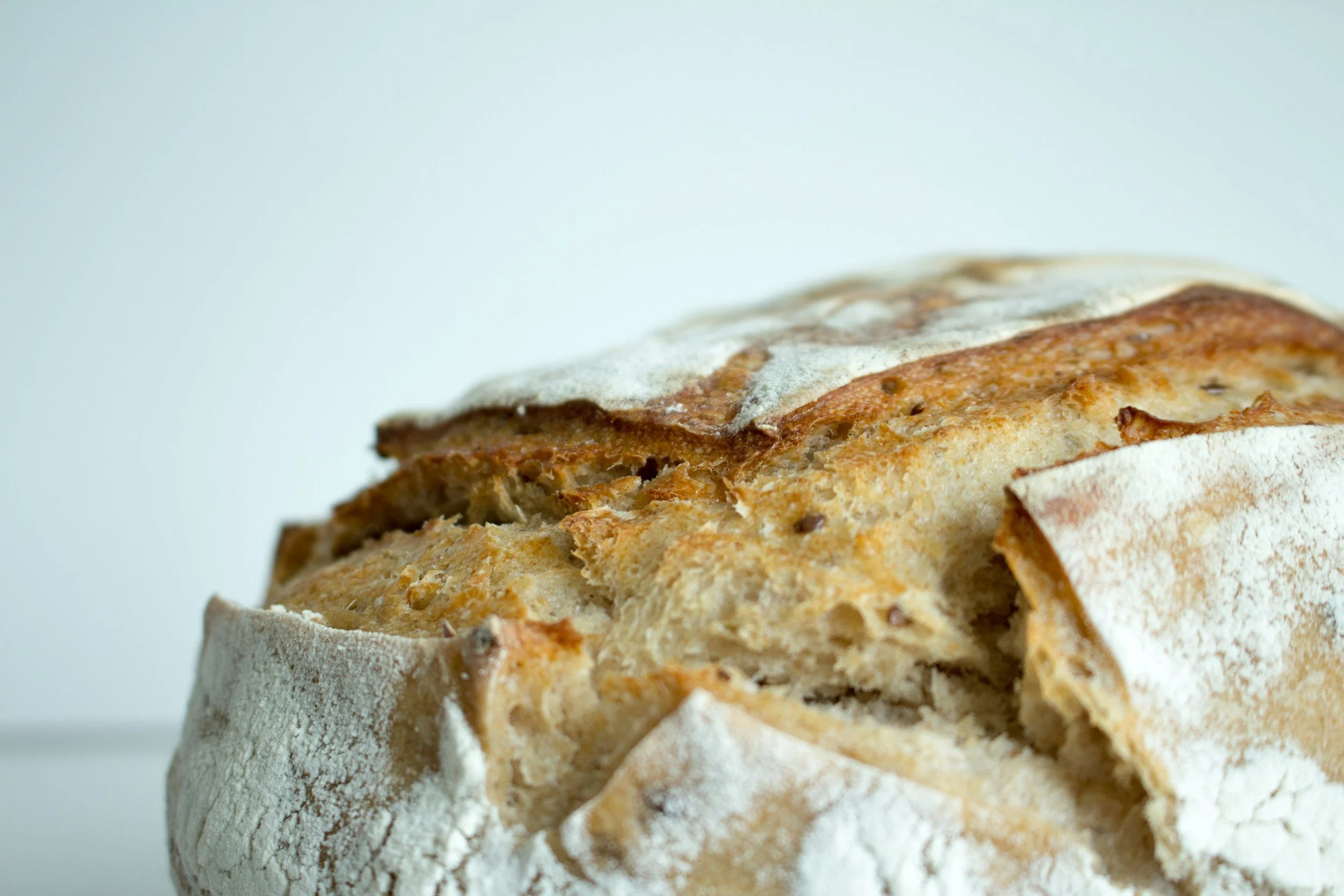 Close-up of a rustic loaf of bread with a crusty exterior and sliced open to reveal a soft, airy interior, dusted with flour.
