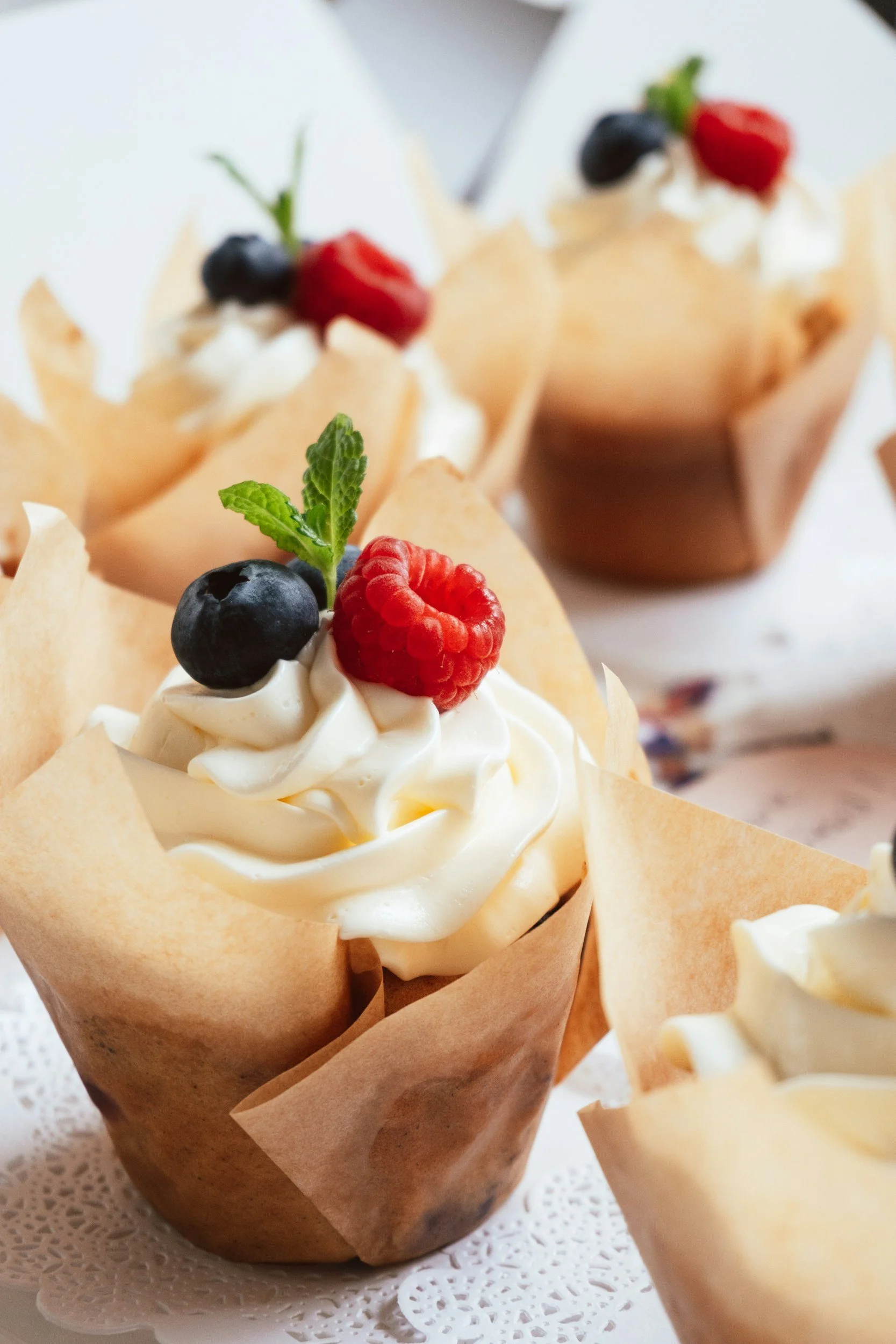 Cupcakes decorated with whipped cream, blueberries, raspberries, and mint, wrapped in parchment paper