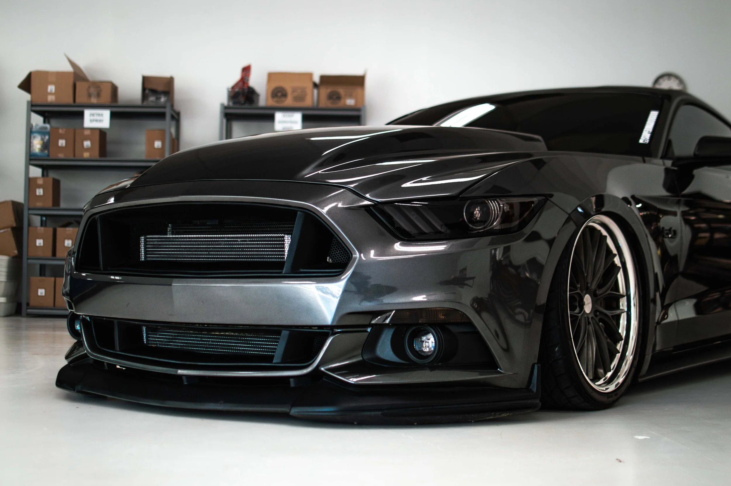 Black sports car with wide wheels parked indoors, with shelves and boxes in the background.