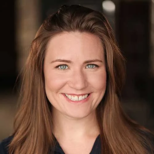 A woman smiling with long brown hair and blue eyes.