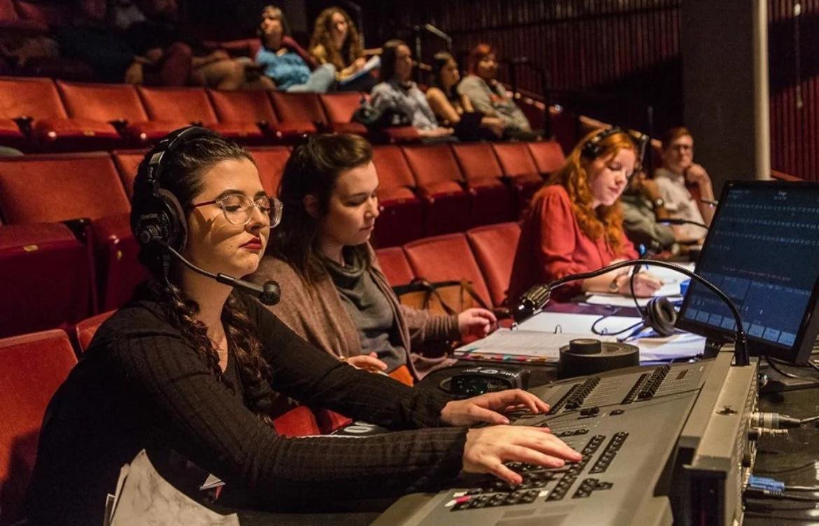 People working as audio or video production crew, some with headphones, in an auditorium with red seats.