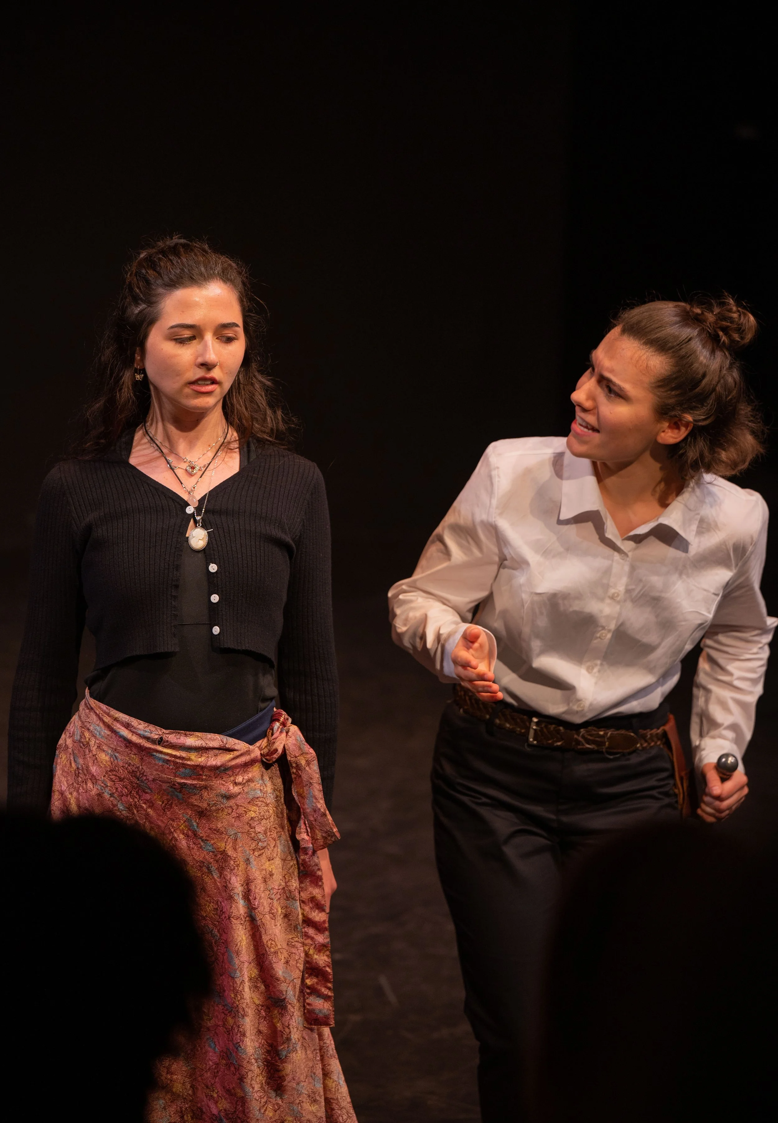 Two women performing on stage, one appears upset and the other looks concerned while holding a microphone.