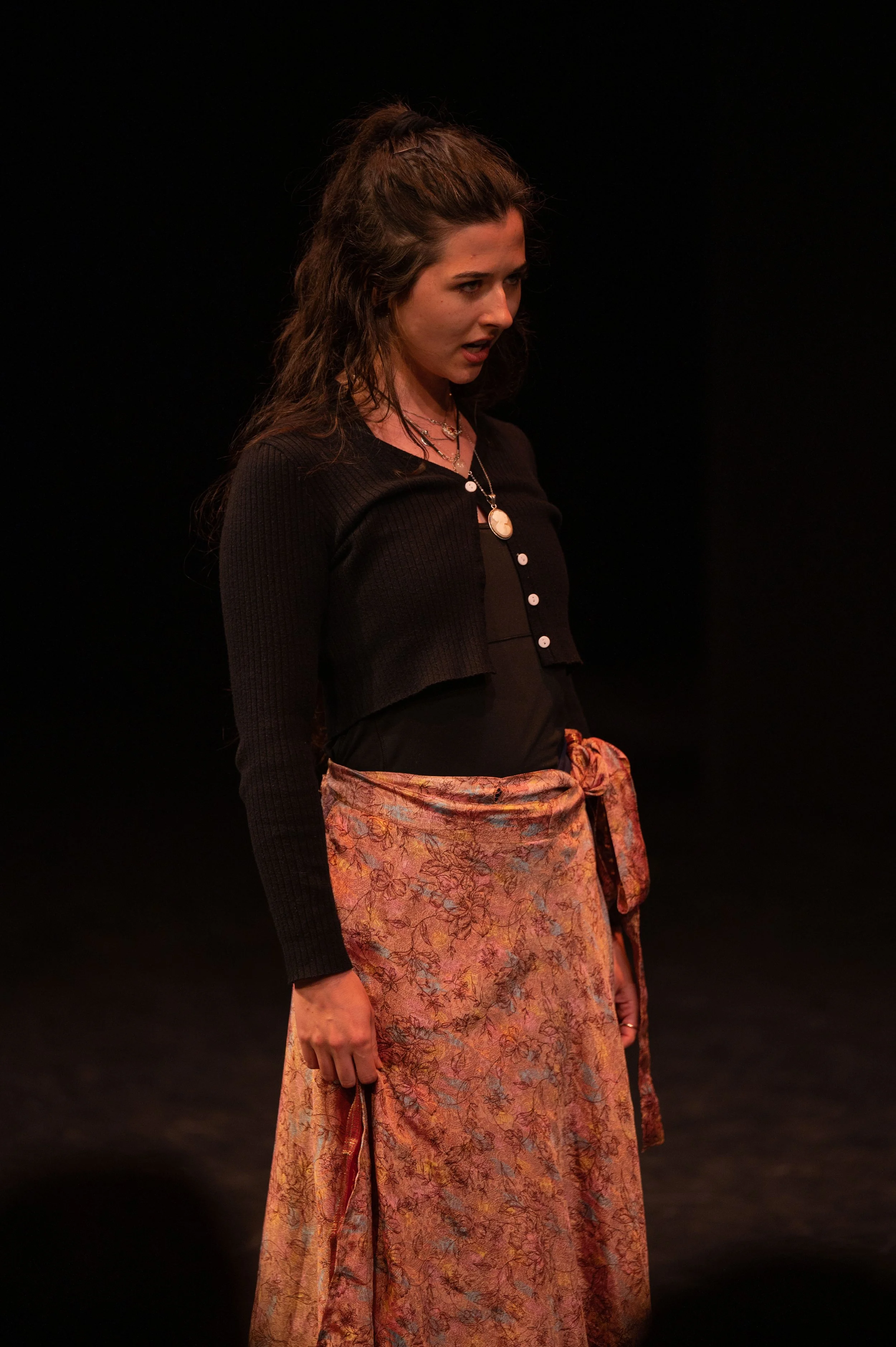 A woman with long, curly hair wearing a black top and a floral pink skirt.