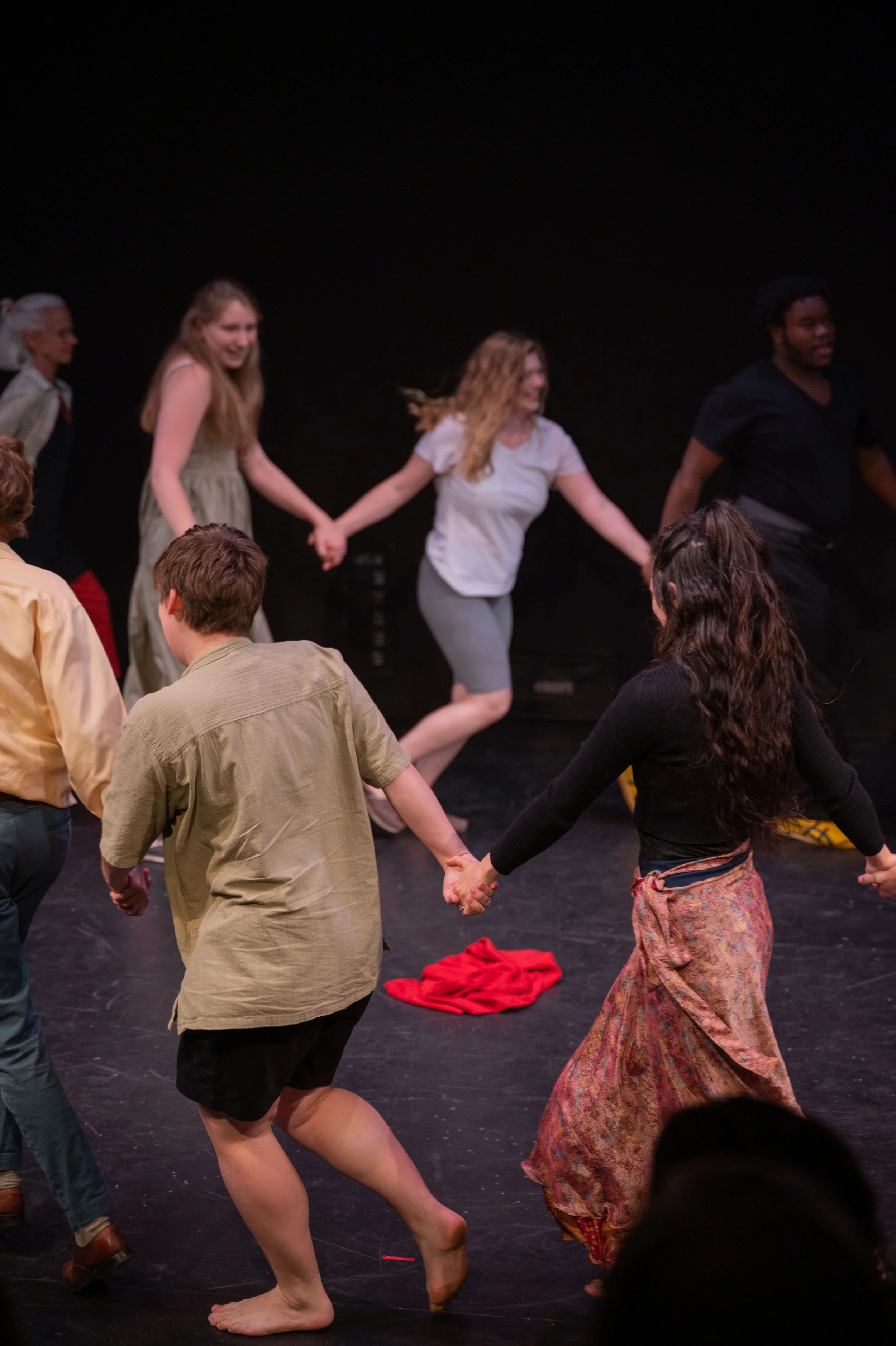 People holding hands and dancing in a circle on a dark stage.