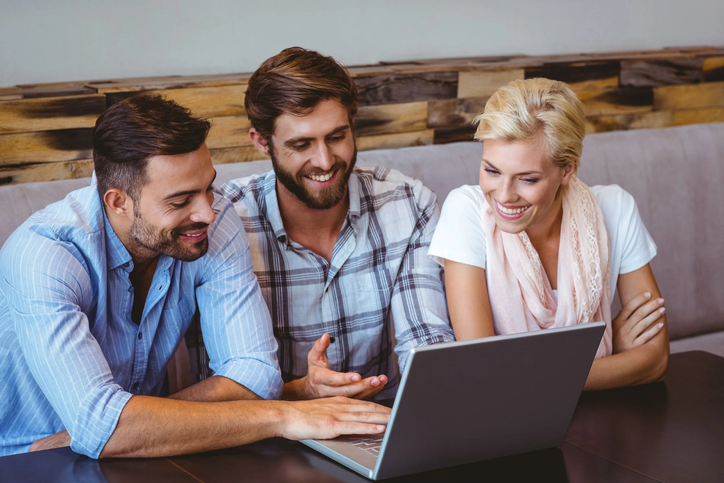 Three people sitting at a table looking at a laptop, smiling and engaging with each other.