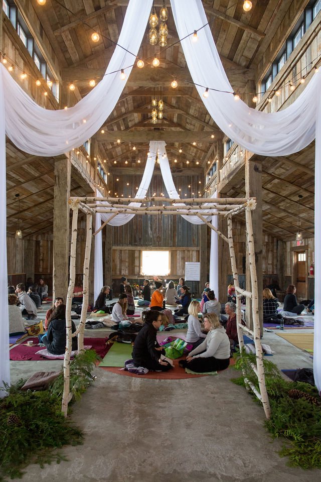 Elegant indoor gathering space with draped white fabric, warm string lights, and people seated on the floor in a decorated hall.