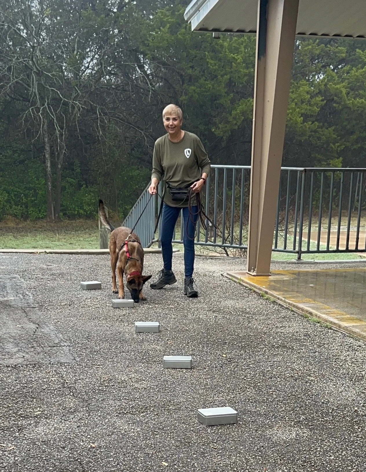 A woman walking a dog on a leash outdoors on a cloudy day, with small white blocks on the ground.