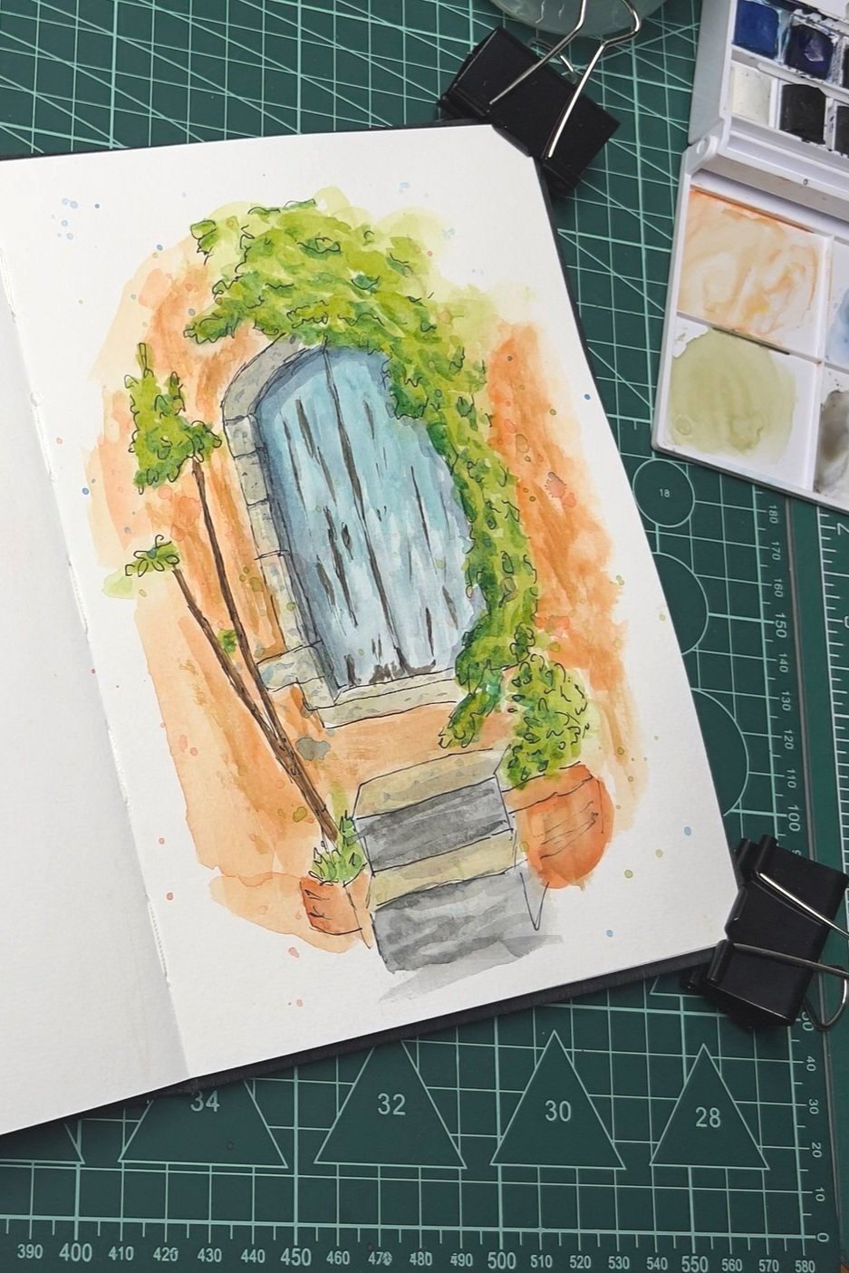 Caderno de esboço sobre superfície com régua, pintura de porta e vegetação.