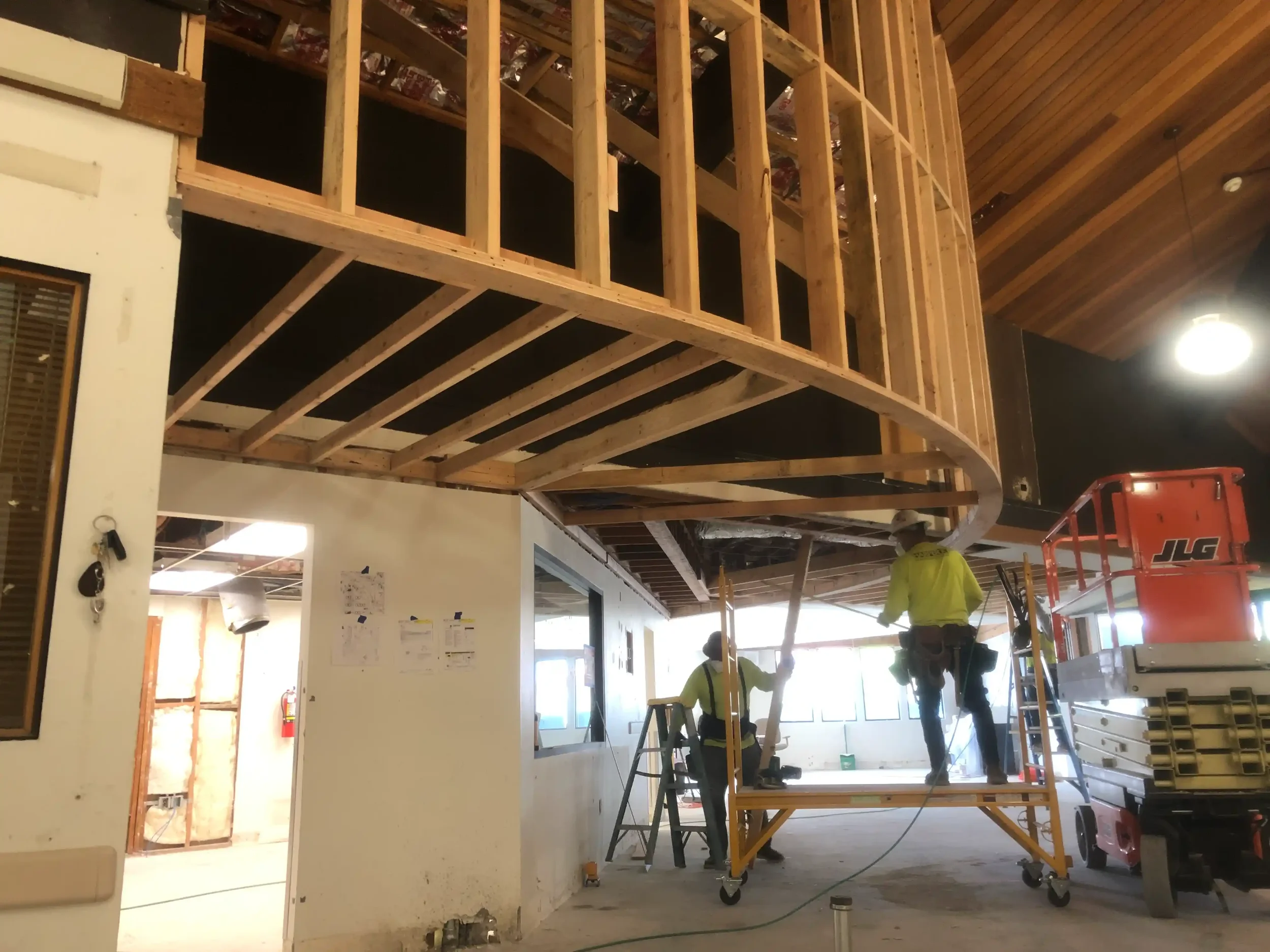 Construction workers working on framing a building with wooden beams and scaffolding inside a partially remodeled interior space.