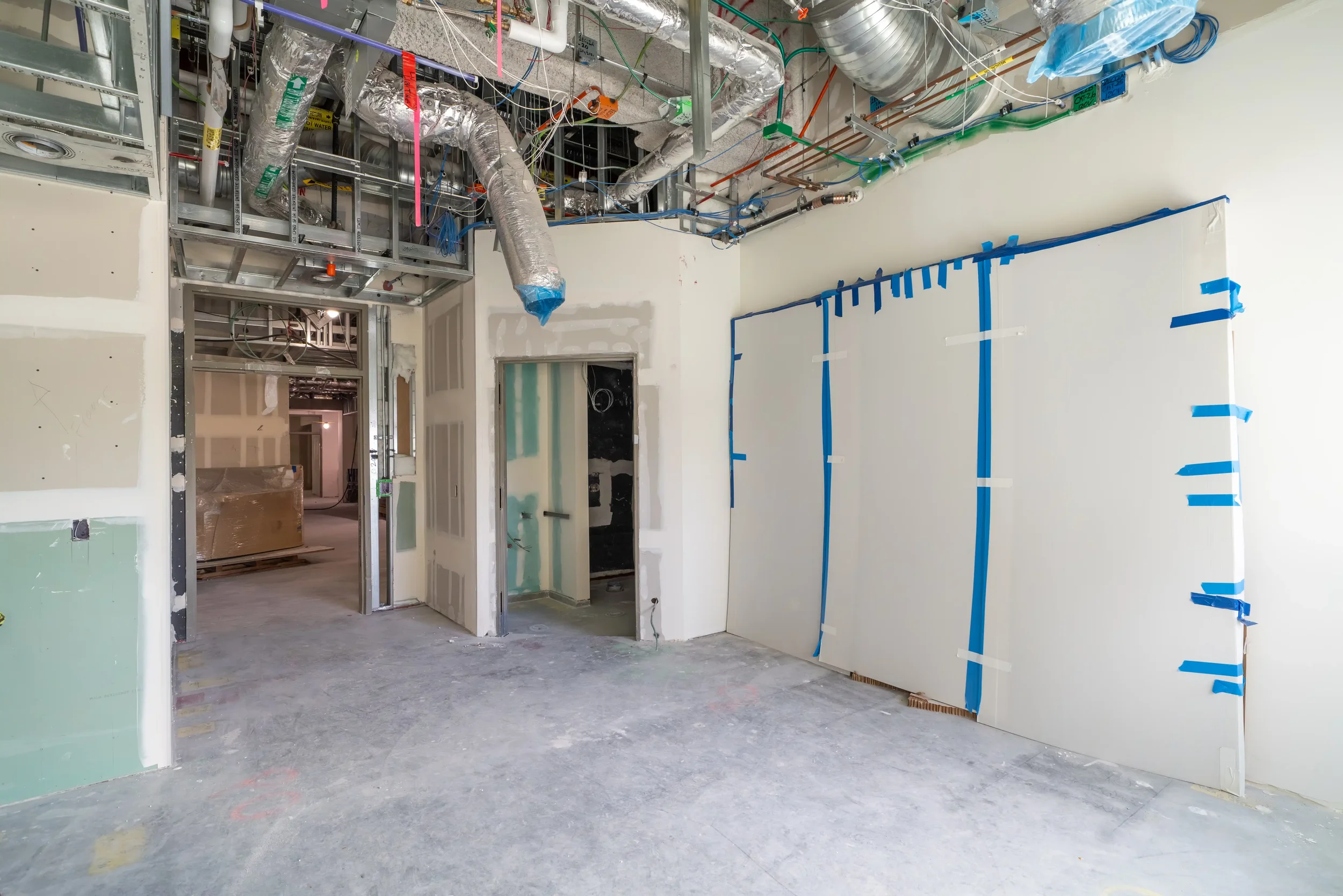 Interior of a building under construction, showing drywall and exposed ductwork, wiring, and framing.