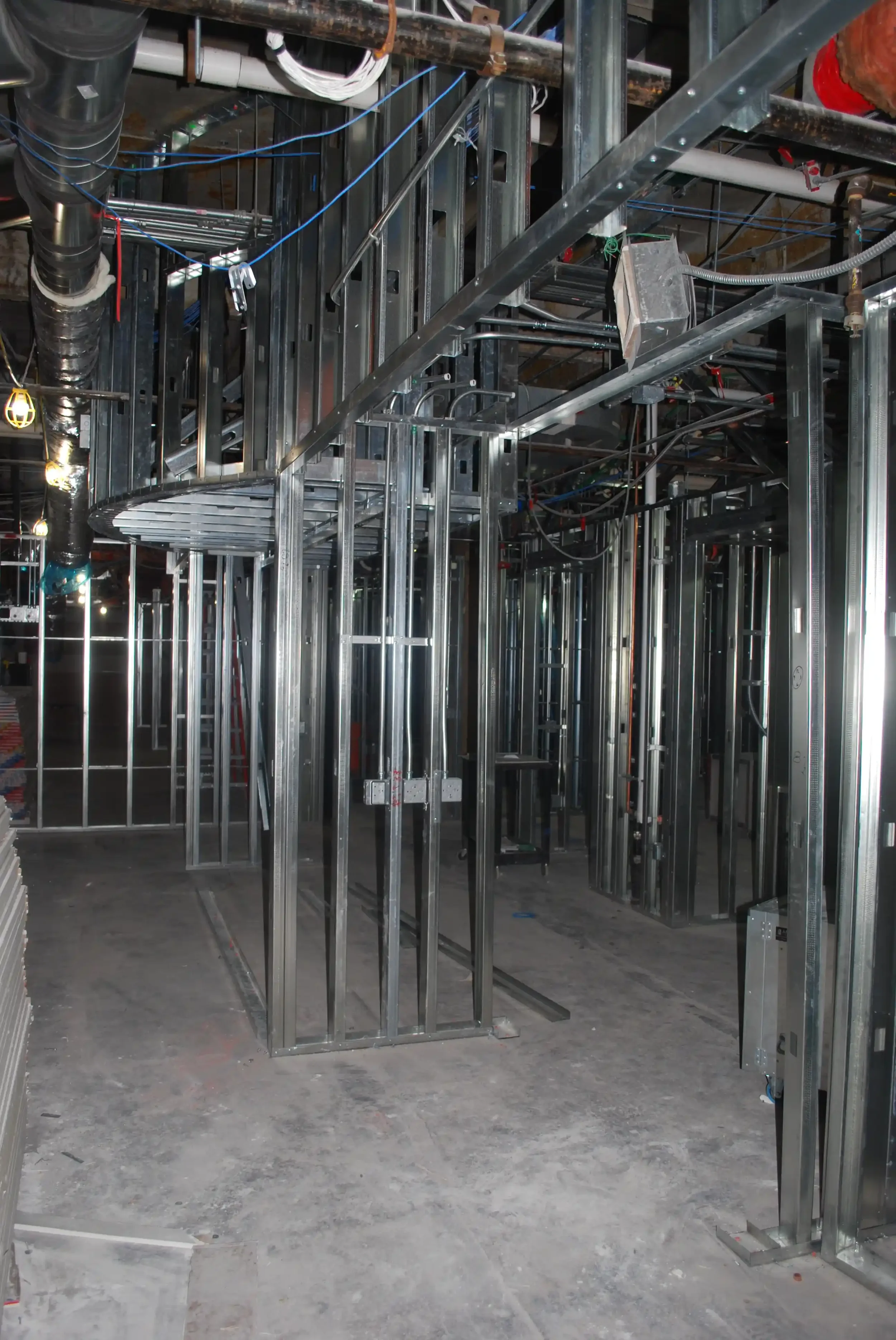 Construction site with metal framing and electrical wiring in progress, showing steel studs and conduit infrastructure.