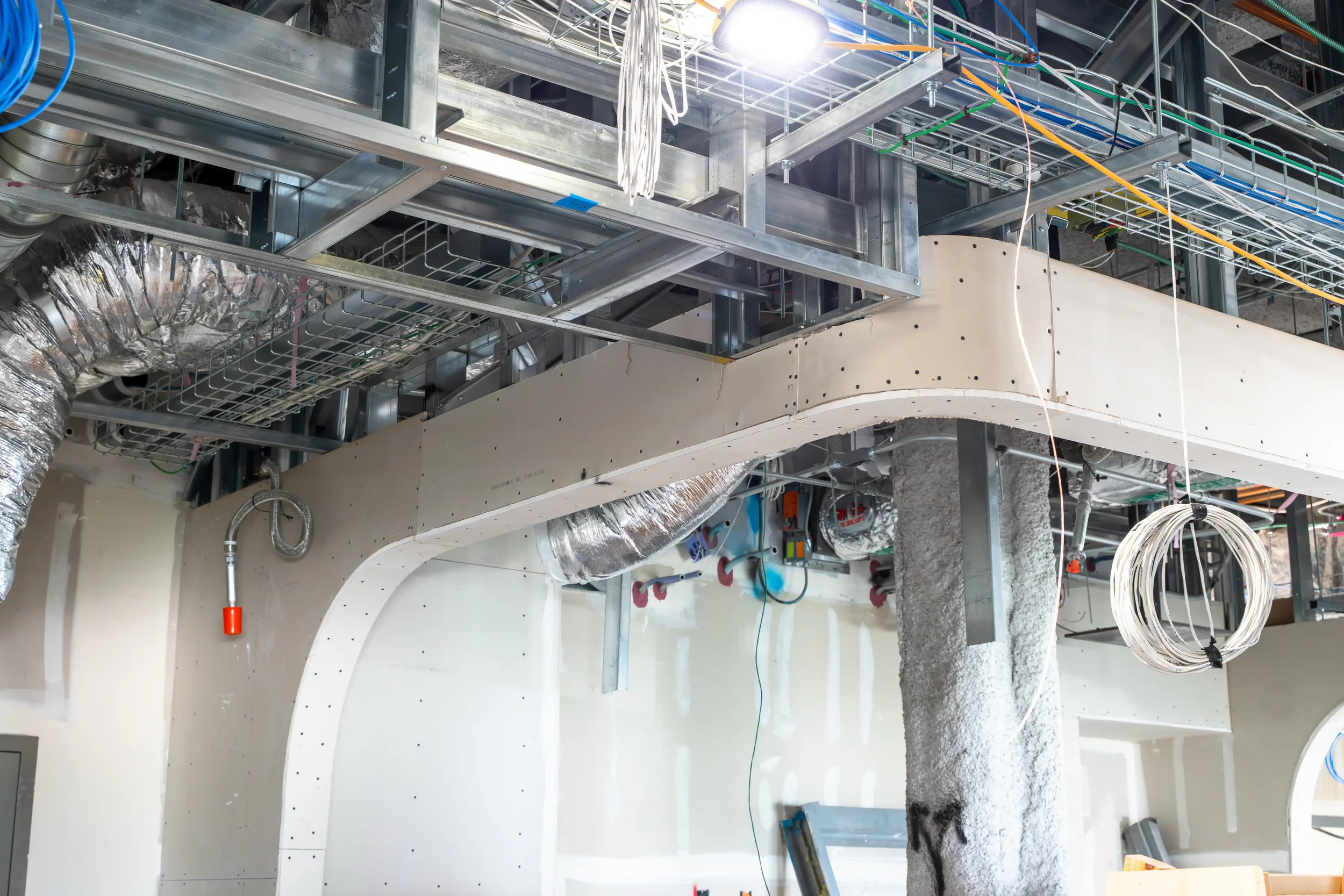 Construction site with metal framework, wiring, ducts, and partially completed walls.