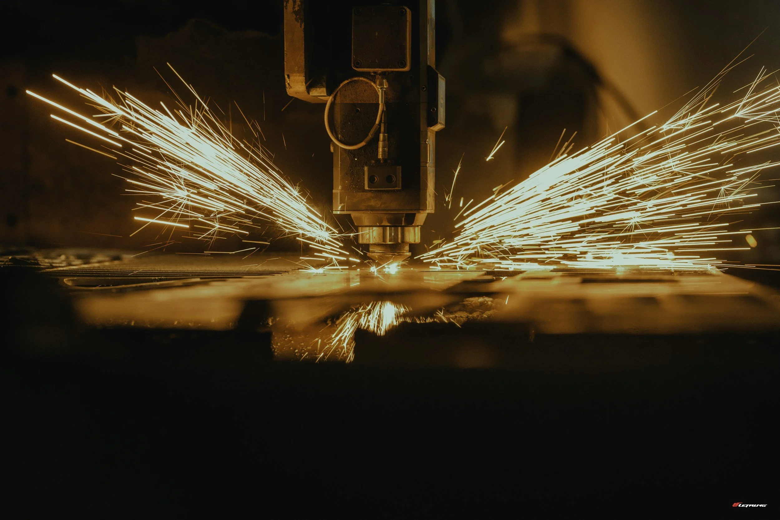 A machine cutting or welding metal with sparks flying in all directions in a dark environment.