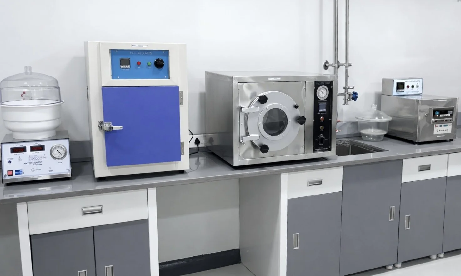 Laboratory equipment, including sterilizer, ultrasonic cleaner, and drying oven, on a stainless steel countertop.