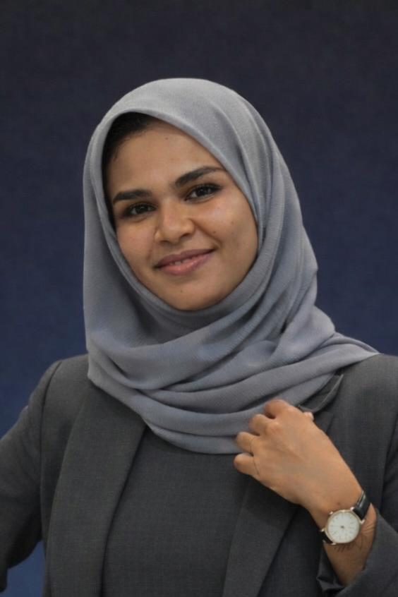 A woman wearing a light gray hijab and a dark gray blazer, smiling confidently against a dark blue background.