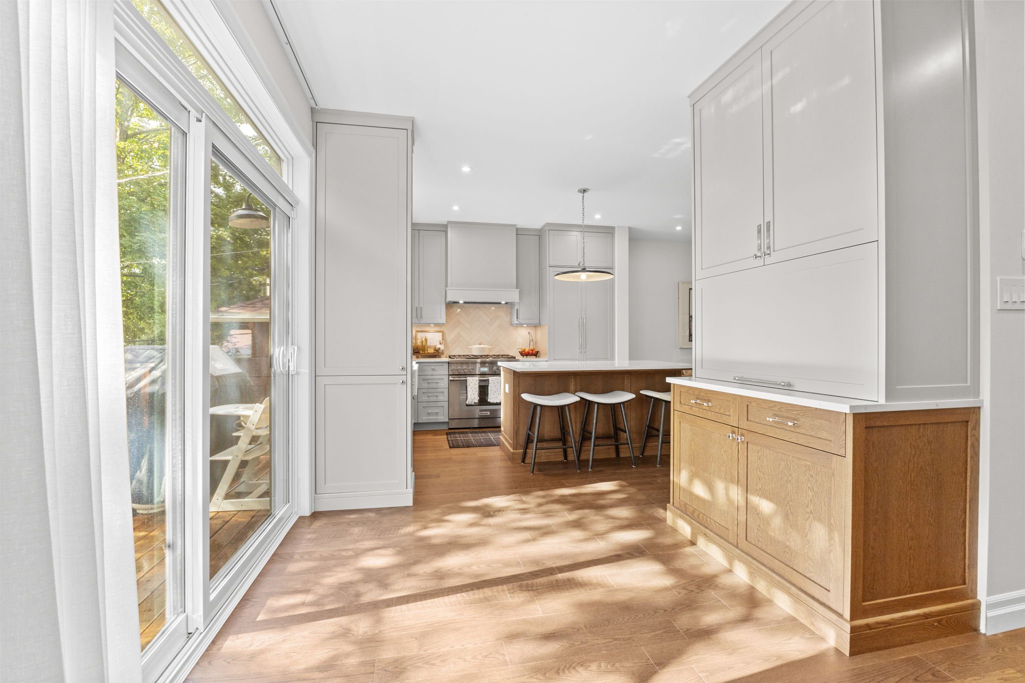 Bright kitchen in a Kanata home featuring white cabinetry, a wood island with bar seating, hardwood flooring, and a sliding glass door bringing in natural light, designed for functional everyday living.