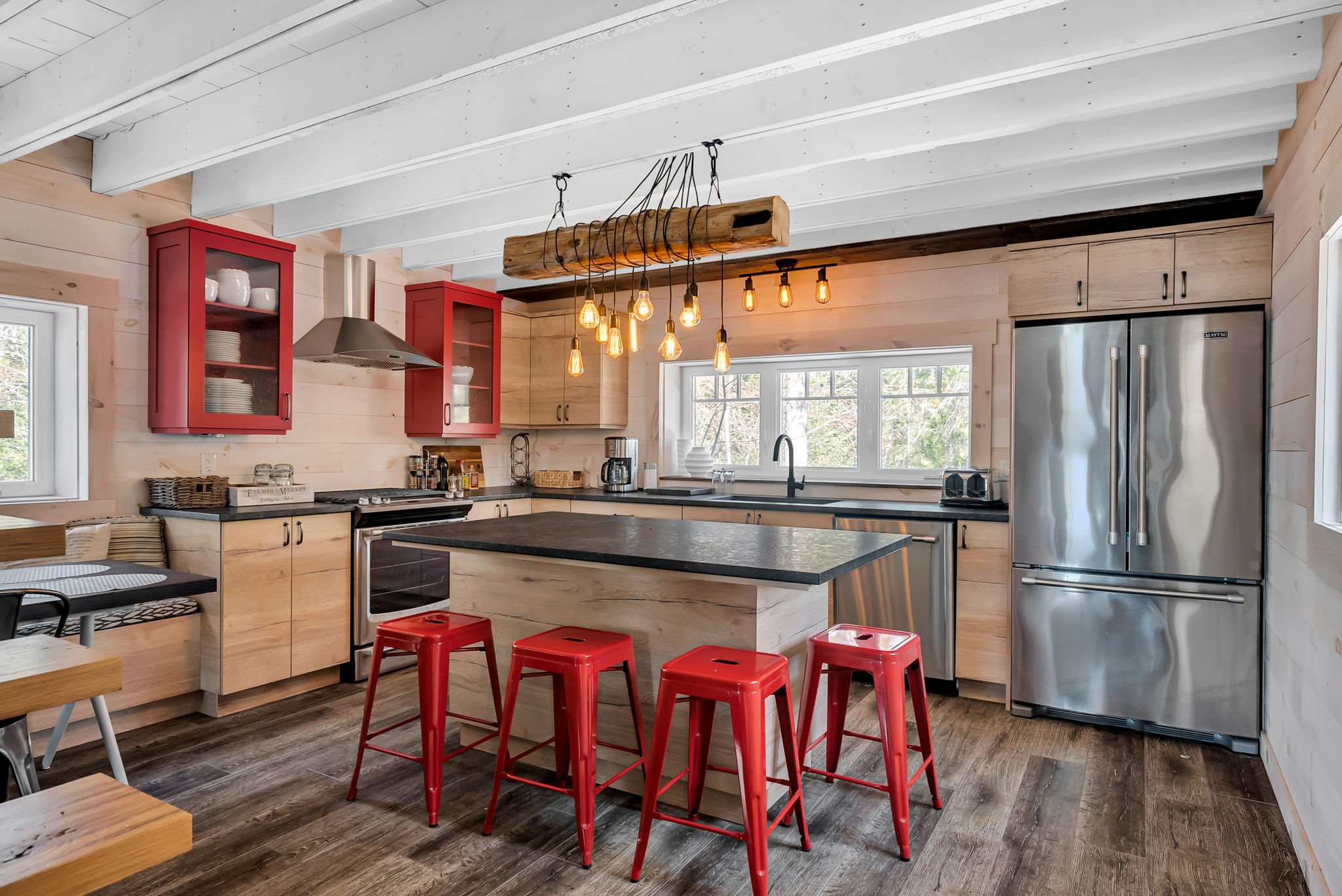 A modern rustic kitchen blending warm wood cabinetry, bold red accents, and a black island, complemented by exposed beams and statement lighting.