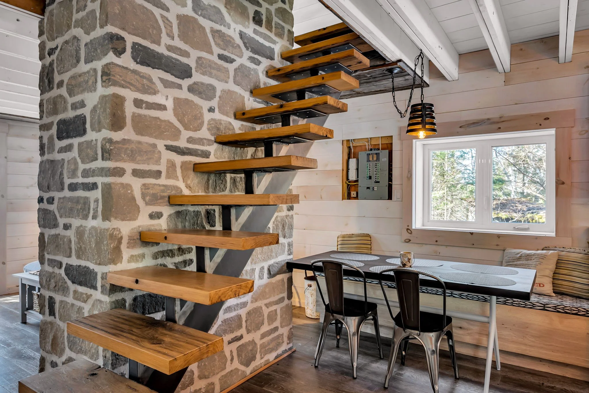 Open-concept interior in a rustic Ontario home featuring a stone fireplace, custom wood staircase, and dining area with views to surrounding trees, blending natural materials with functional design, built by Centennial Construction Management,