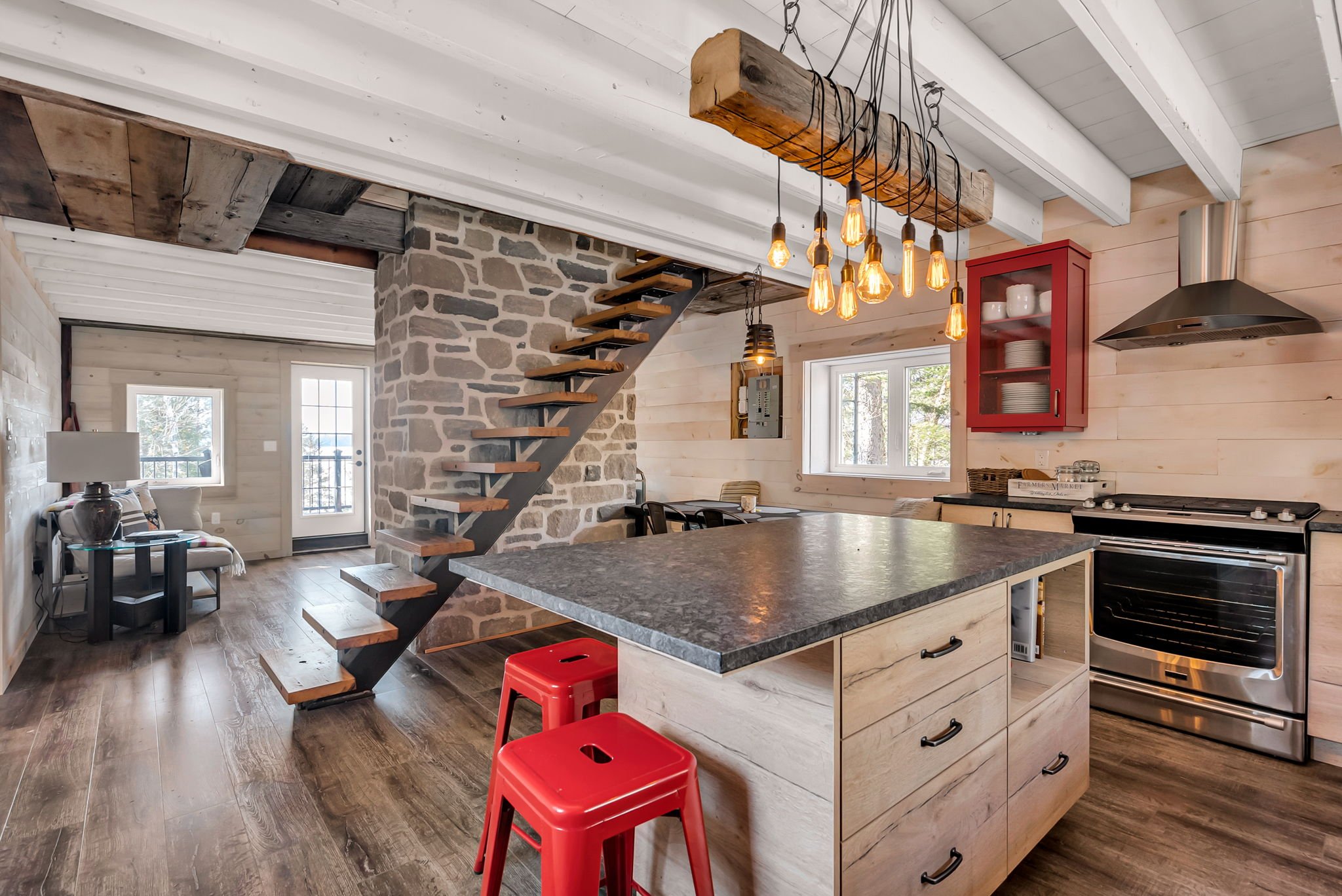 Rustic modern kitchen interior in Ontario featuring wood-paneled walls, a stone fireplace, granite island with seating, and a custom wood staircase, blending natural materials with modern appliances and warm lighting, built by Centennial Construction