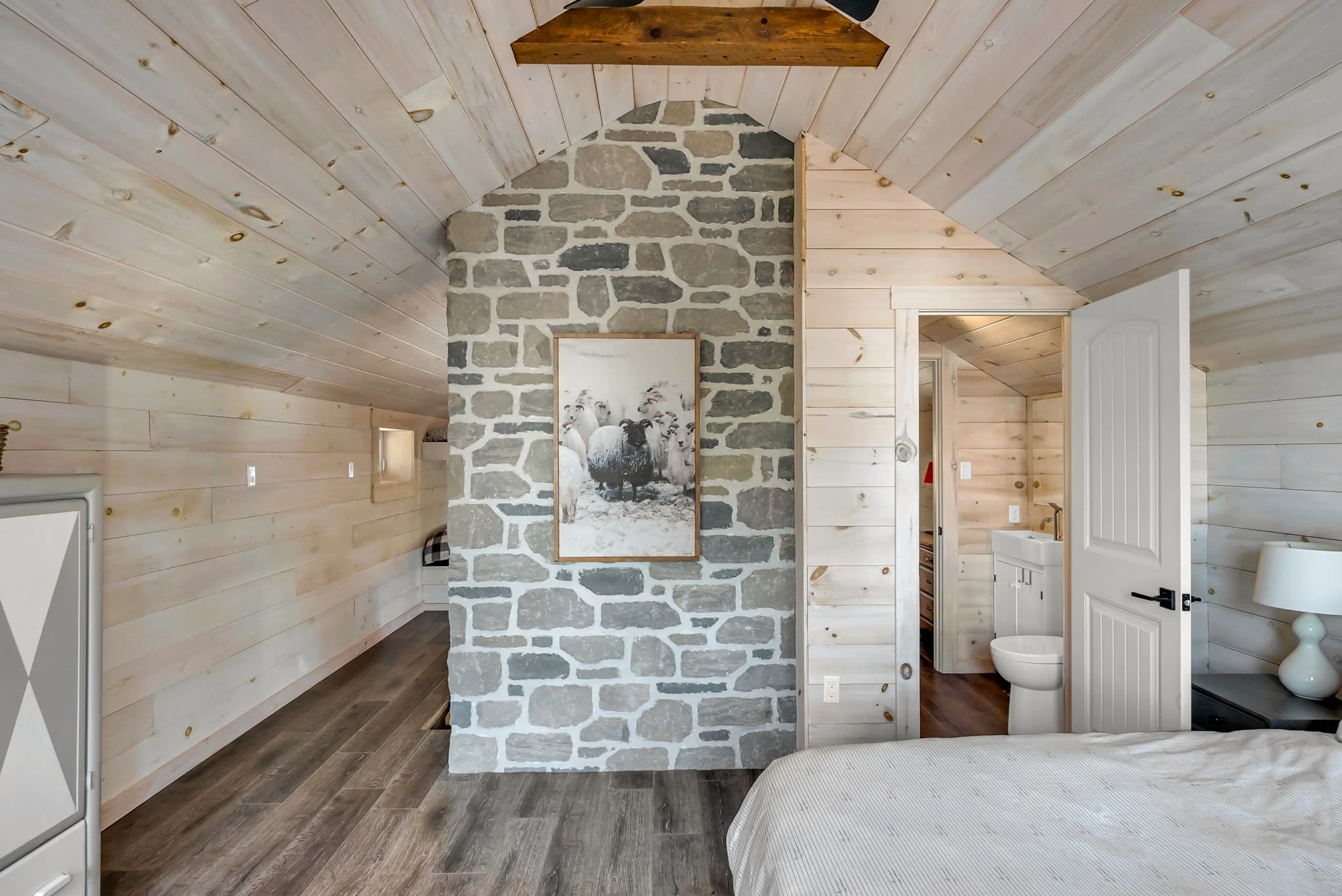 Rustic bedroom interior in an Ontario home featuring wood-paneled walls and ceiling, a stone accent wall, and direct access to an ensuite bathroom, blending natural materials with functional layout design
