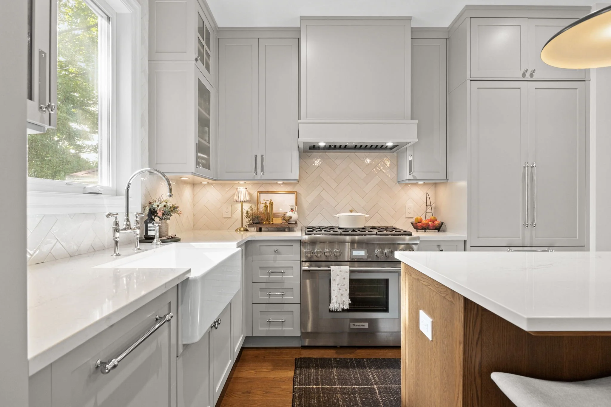 Modern kitchen with gray cabinets, white countertops, stainless steel oven, herringbone tile backsplash, window above sink, and wooden island