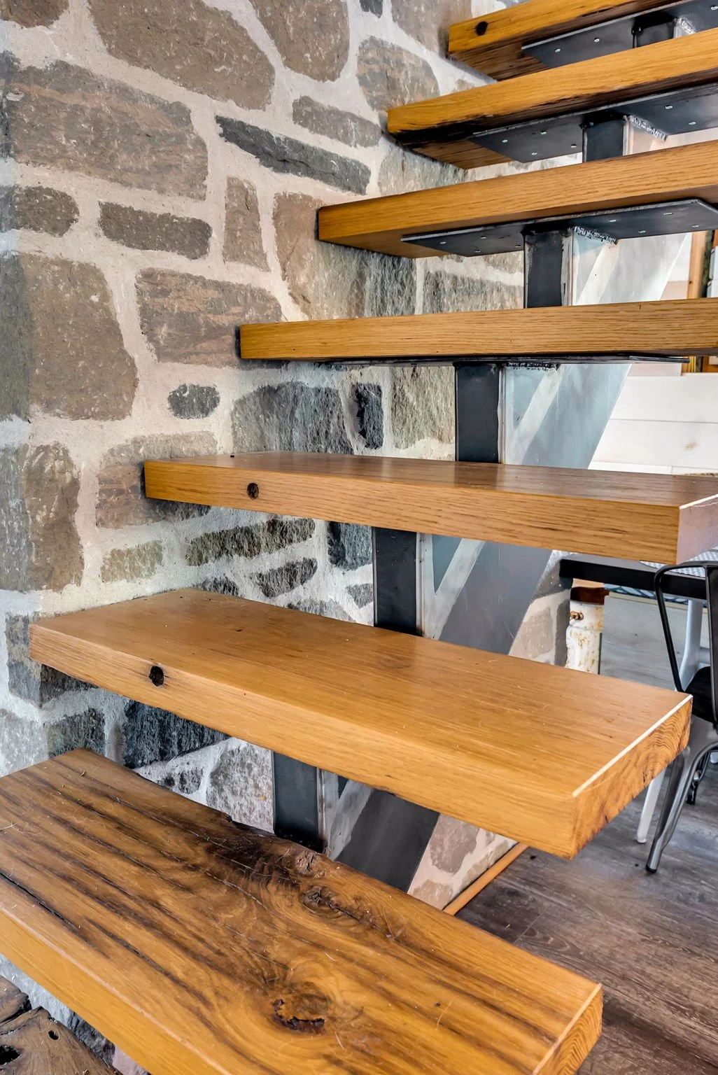 Custom wood staircase with wide treads mounted against a natural stone feature wall, showcasing clean structural design and material contrast in this Ottawa build by Centennial Construction Management, a professional builder operating under Ontario’s