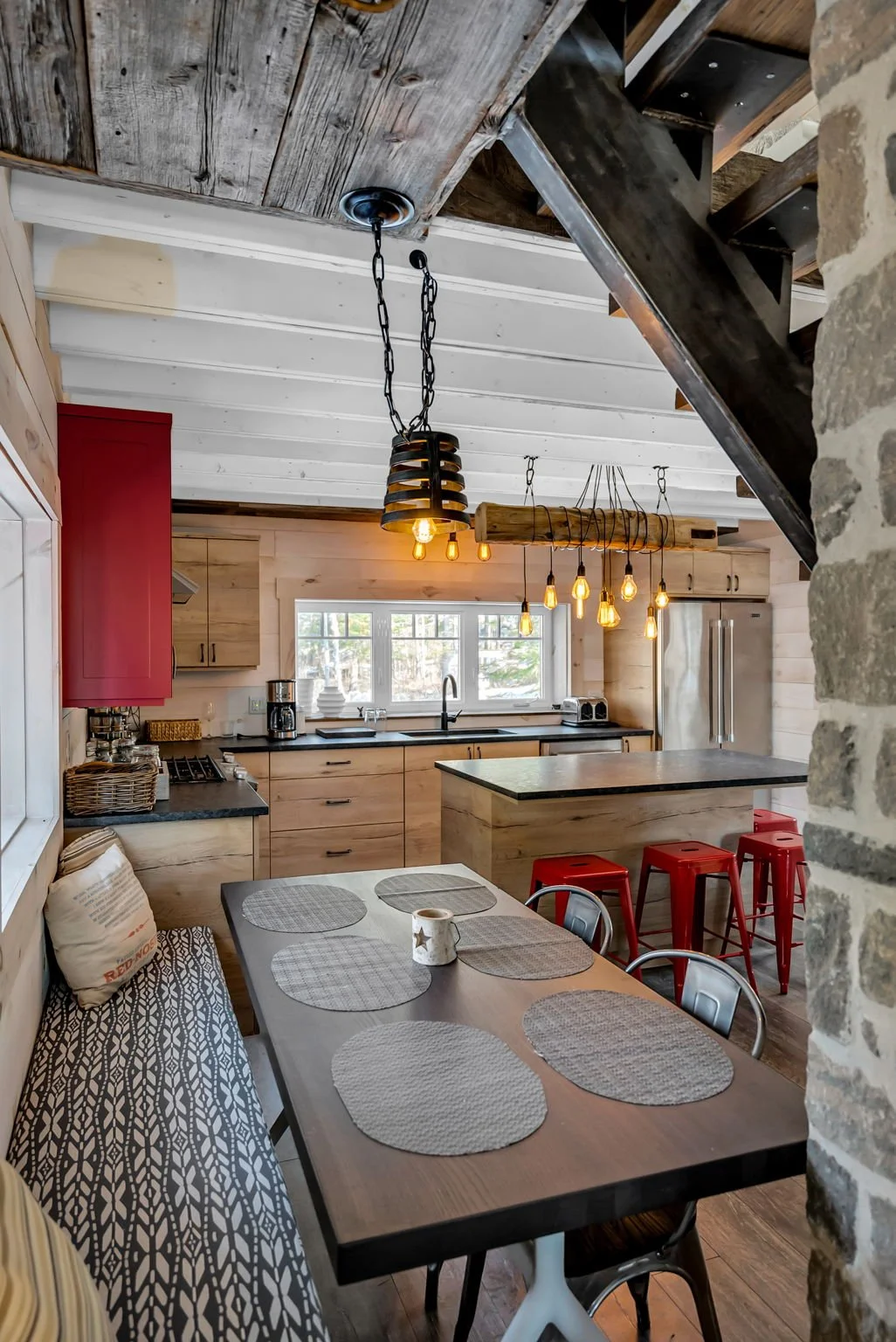 Rustic kitchen with wood-paneled walls, pendant lighting, and a dining table with placemats and chairs.