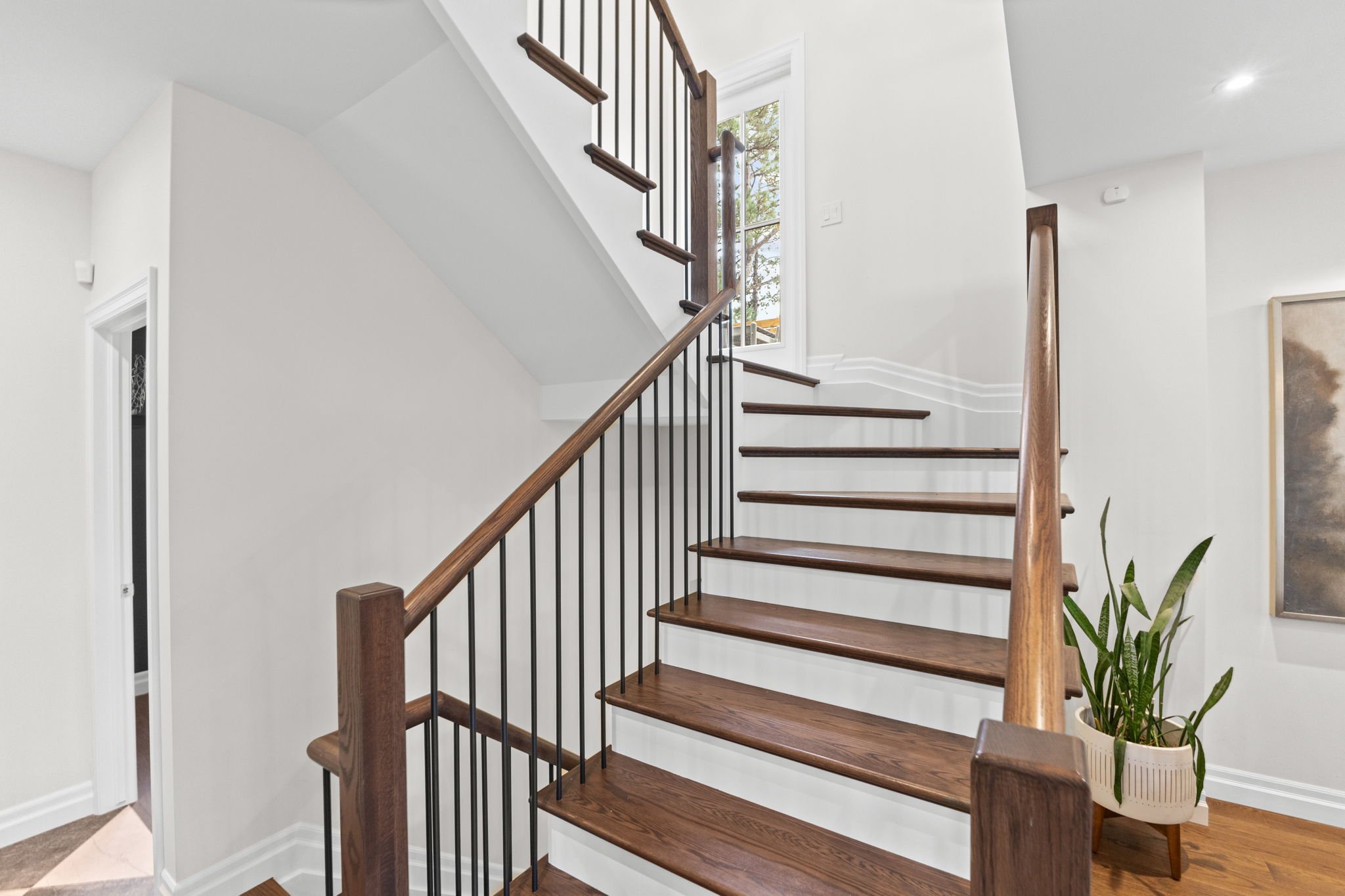 Custom wood staircase in a Rockcliffe Park home featuring black metal balusters, a wood handrail, and a clean white interior, complemented by natural elements and thoughtful detailing.
