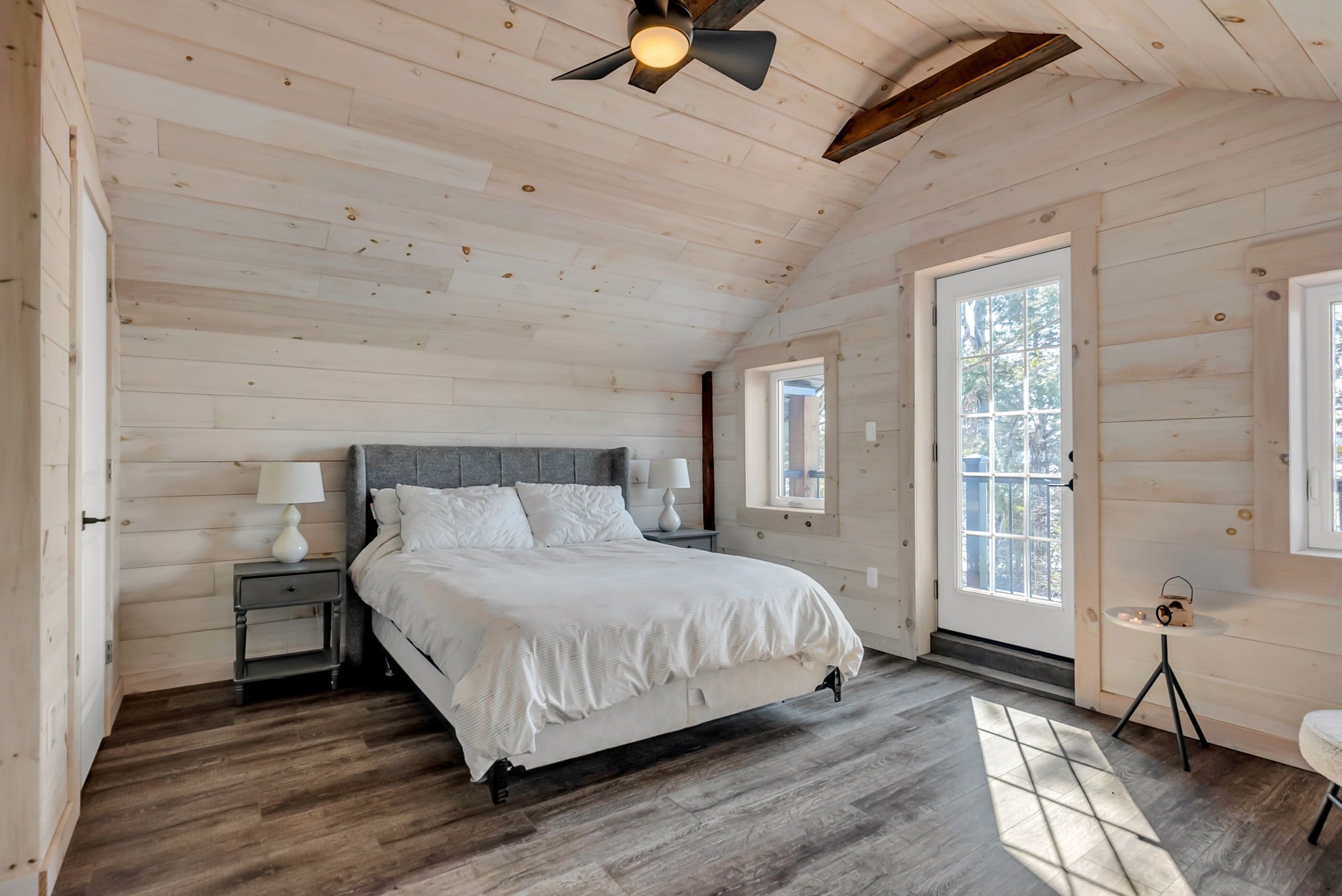 Cozy bedroom in an Ontario home featuring wood-paneled walls and ceiling, a queen bed with neutral finishes, bedside lighting, and ample natural light, creating a warm and functional retreat by Centennial Construction Management.