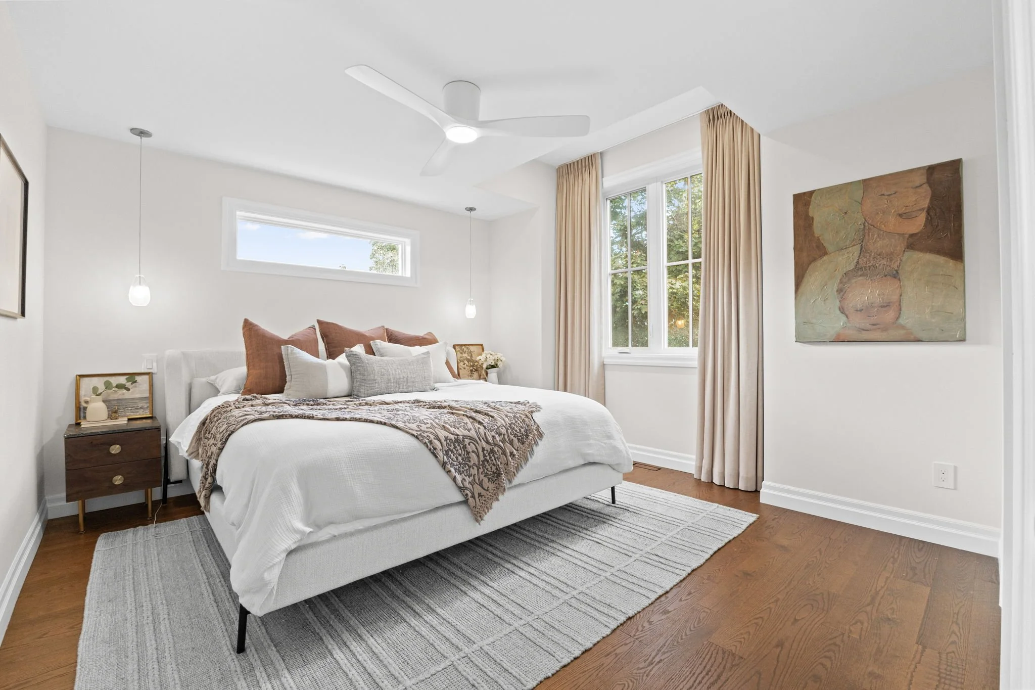 Bright modern bedroom in a Manor Park home featuring a white bed with layered bedding, wood nightstands, pendant lighting, and soft natural light through window treatments, creating a calm and refined retreat.