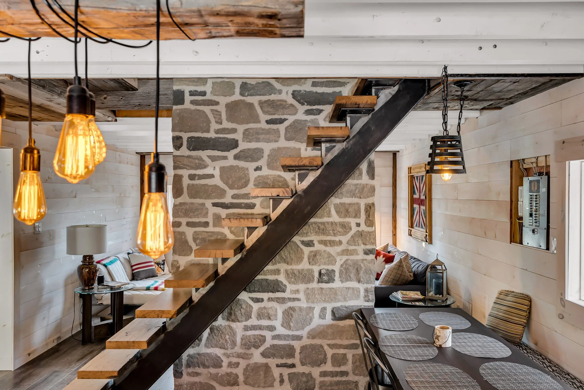 Rustic interior in an Ontario home featuring a natural stone wall, custom wood staircase, and open dining and seating area with Edison bulb lighting, blending warmth, texture, and thoughtful design by Centennial Construction Management.