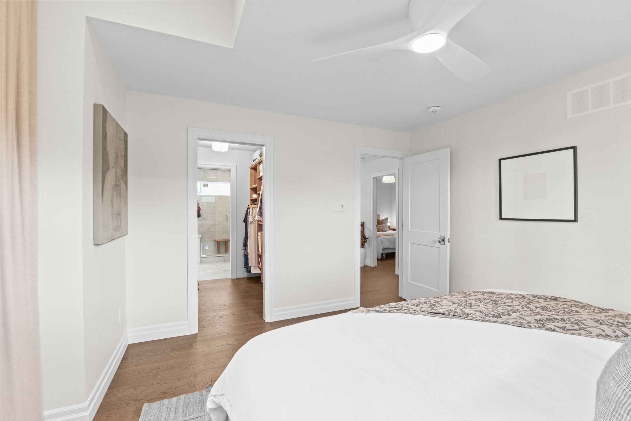 Primary bedroom in an Ottawa home featuring hardwood flooring, a ceiling fan, and direct access to a walk-in closet and ensuite bathroom, designed for comfort, functionality, and seamless everyday living.