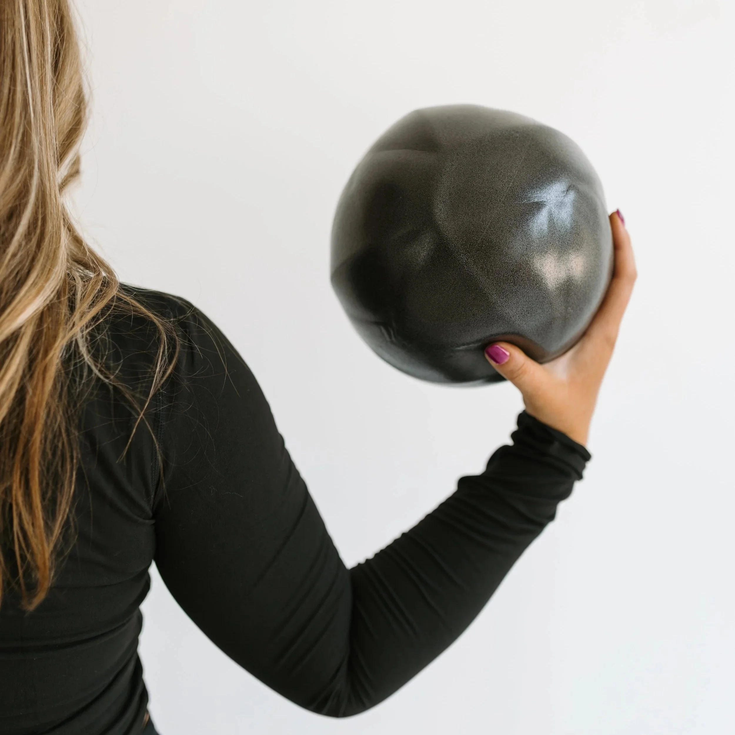 Photograph of a person with long blonde hair holding an exercise ball that is used during the group reformer pilates classes at Worth It: A Reformer Pilates Studio located in Keller Texas, near Dallas, Texas and Fort Worth, Texas.
