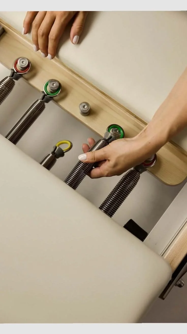 Photograph of hands adjusting springs in the spring well on a luxury reformer used during the group reformer pilates classes at Worth It: A Reformer Pilates Studio located in Keller Texas, near Dallas, Texas and Fort Worth, Texas. The studio houses 1