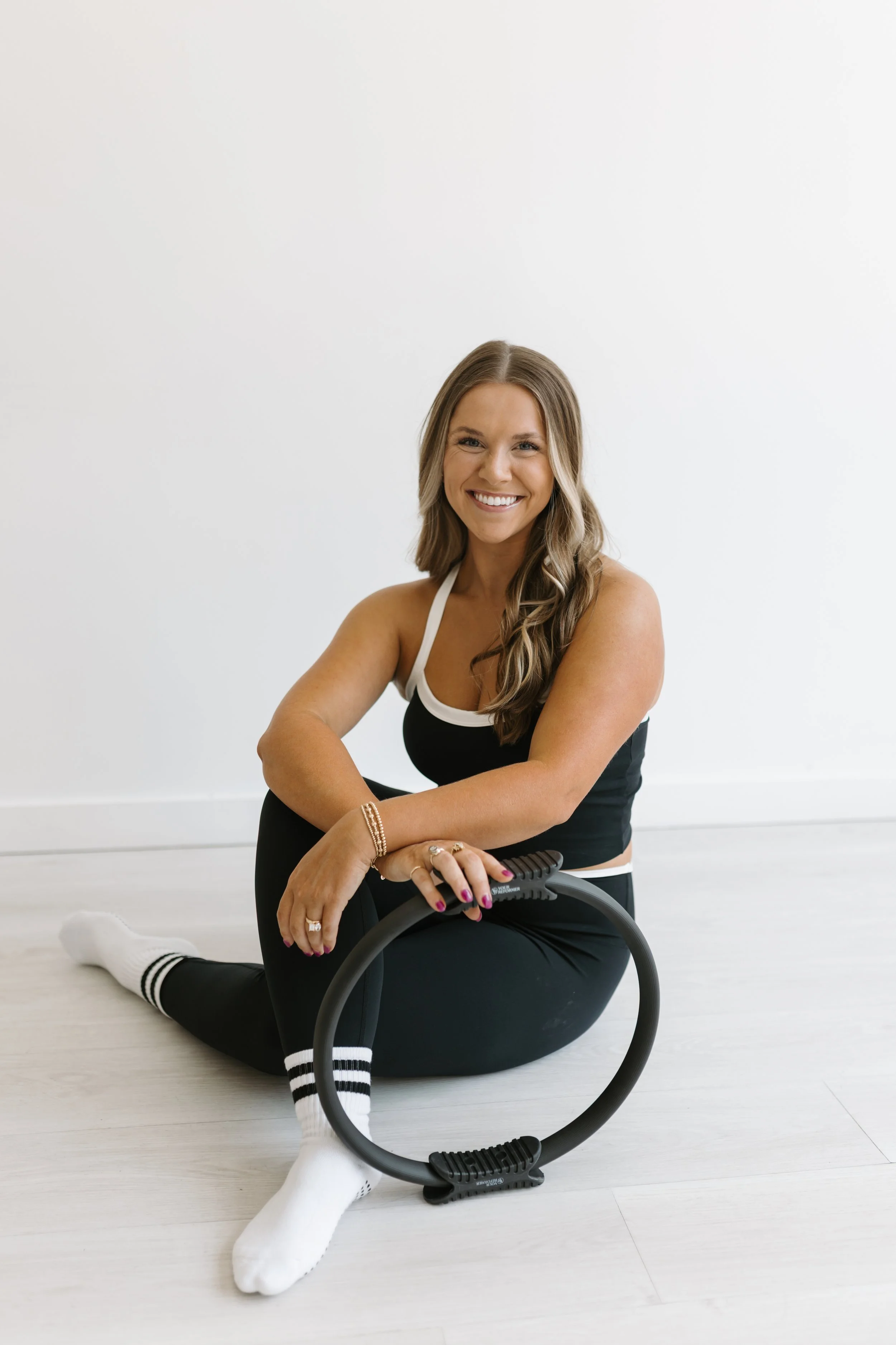 Photograph of Georgia May, the founder of Worth It: A Reformer Pilates Studio in Keller, Texas (Forth Worth, Texas) , smiling in the pilates studio with a pilates ring.