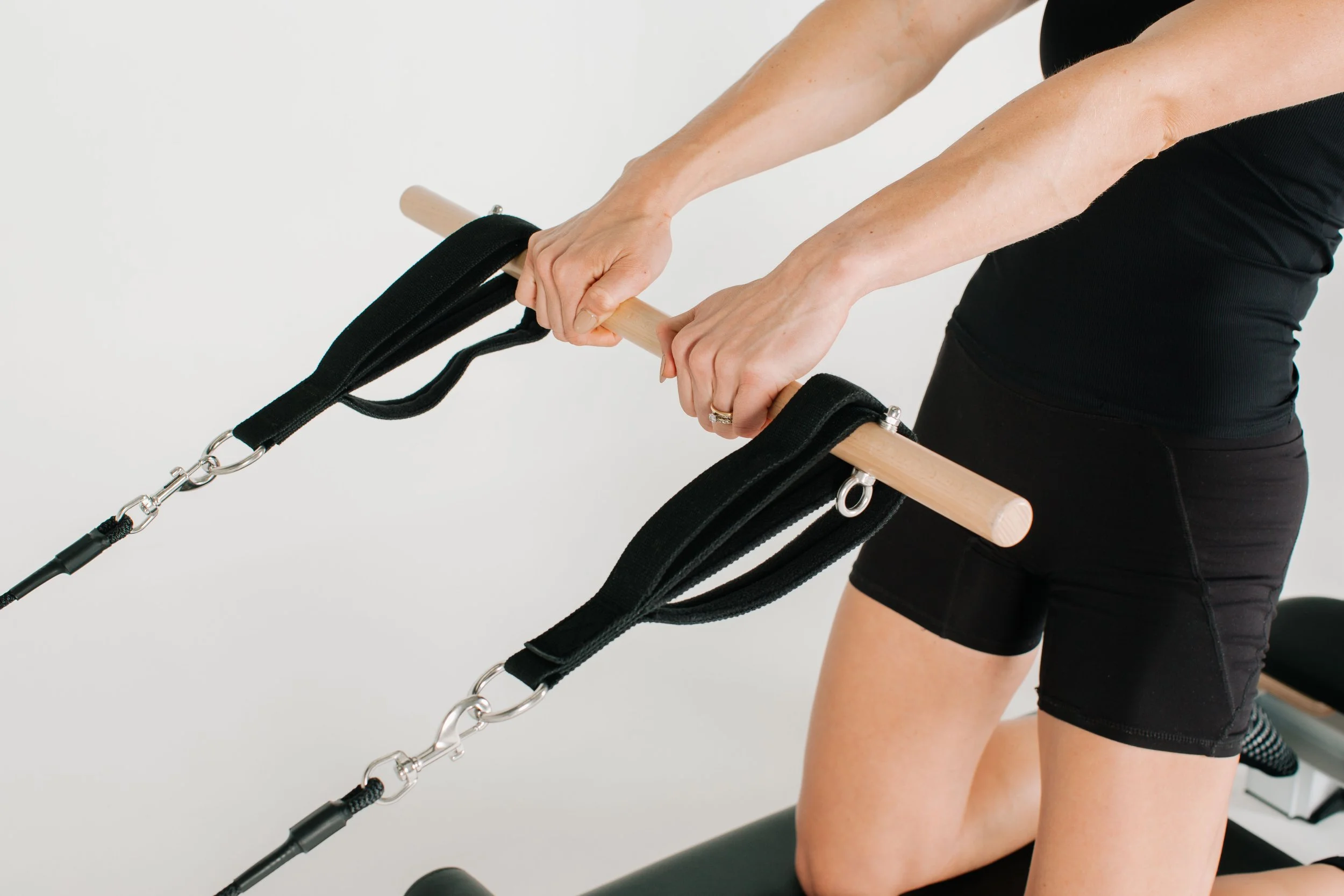 Photograph of tan individual using the straps and wooden bar on the luxury reformer used during the group reformer pilates classes at Worth It: A Reformer Pilates Studio located in Keller Texas, near Dallas, Texas and Fort Worth, Texas. The studio ho