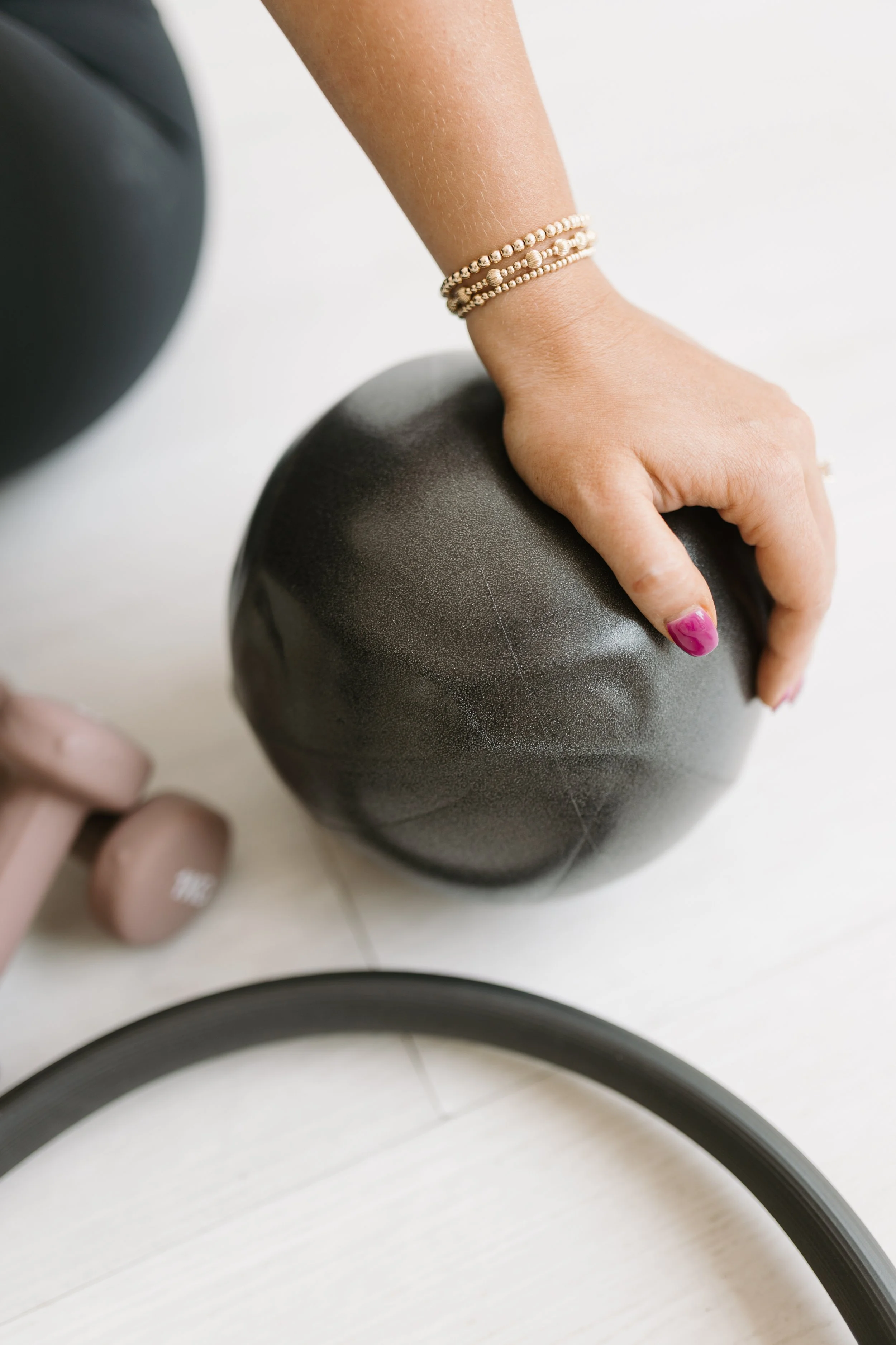 Photograph of workout equipment used during the group reformer pilates classes at Worth It: A Reformer Pilates Studio located in Keller Texas, near Dallas, Texas and Fort Worth, Texas. There is a hand with pink nail polish placed on an exercise ball.