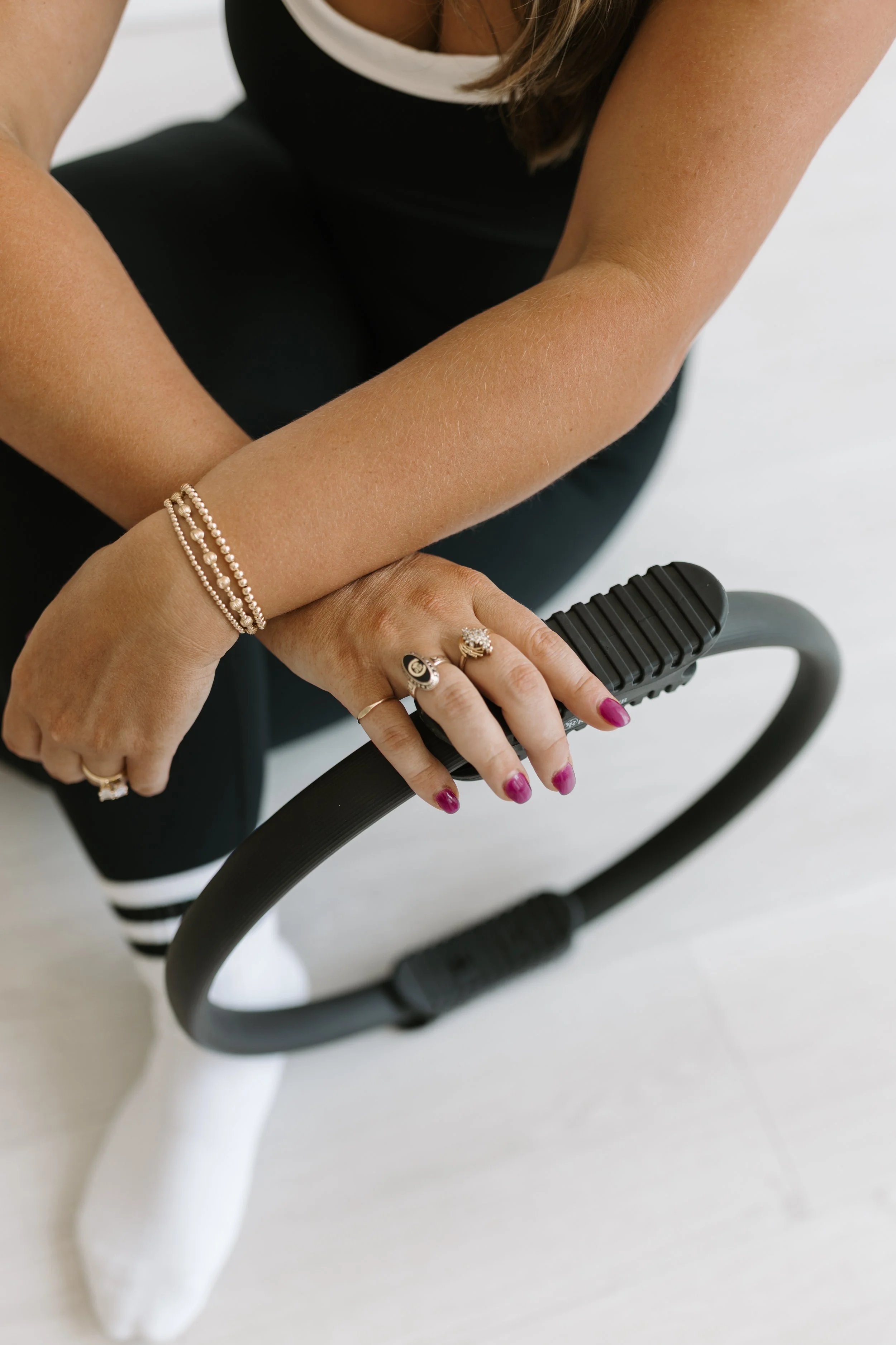 A birds eye photograph of someone in black workout clothes and pink nail polish holding a pilates ring at Worth It: A Reformer Pilates Studio located in Keller Texas, near Dallas, Texas and Fort Worth, Texas.