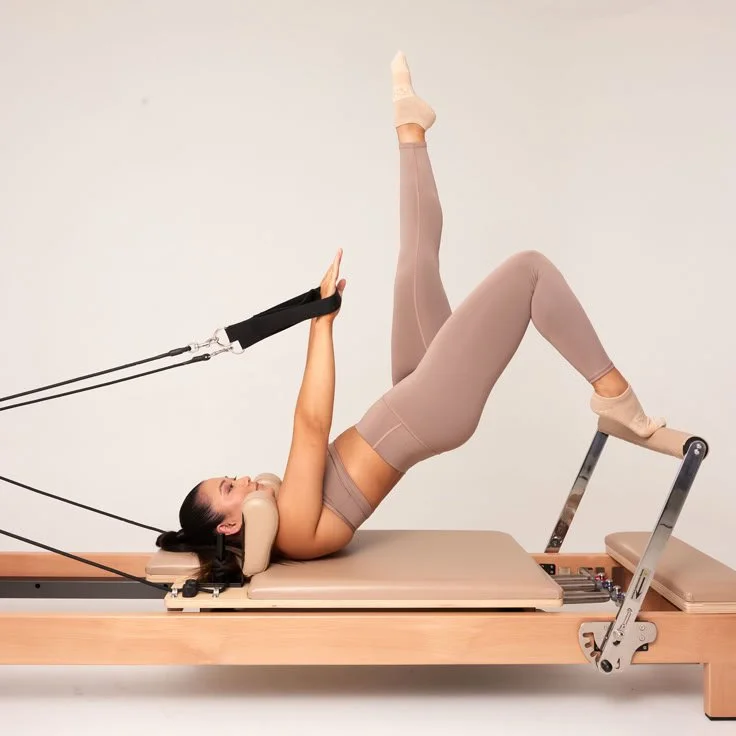 A woman performing a pilates pose on a Pilates reformer machine, with her body in an elevated bridge with one leg lifted to 90 degrees at Worth It: A Reformer Pilates Studio located in Keller Texas, near Dallas, Texas and Fort Worth, Texas.