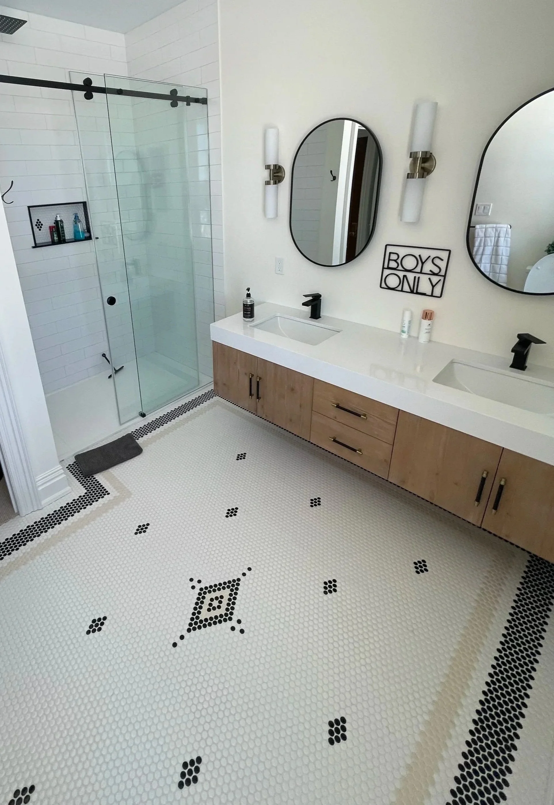 Modern bathroom with a glass-enclosed shower, double vanity with two mirrors, and decorative black and white tile flooring.  Tile Work and Contractor Kawartha Lakes, GTA, Muskokas. Custom tile work and bathroom renovation.