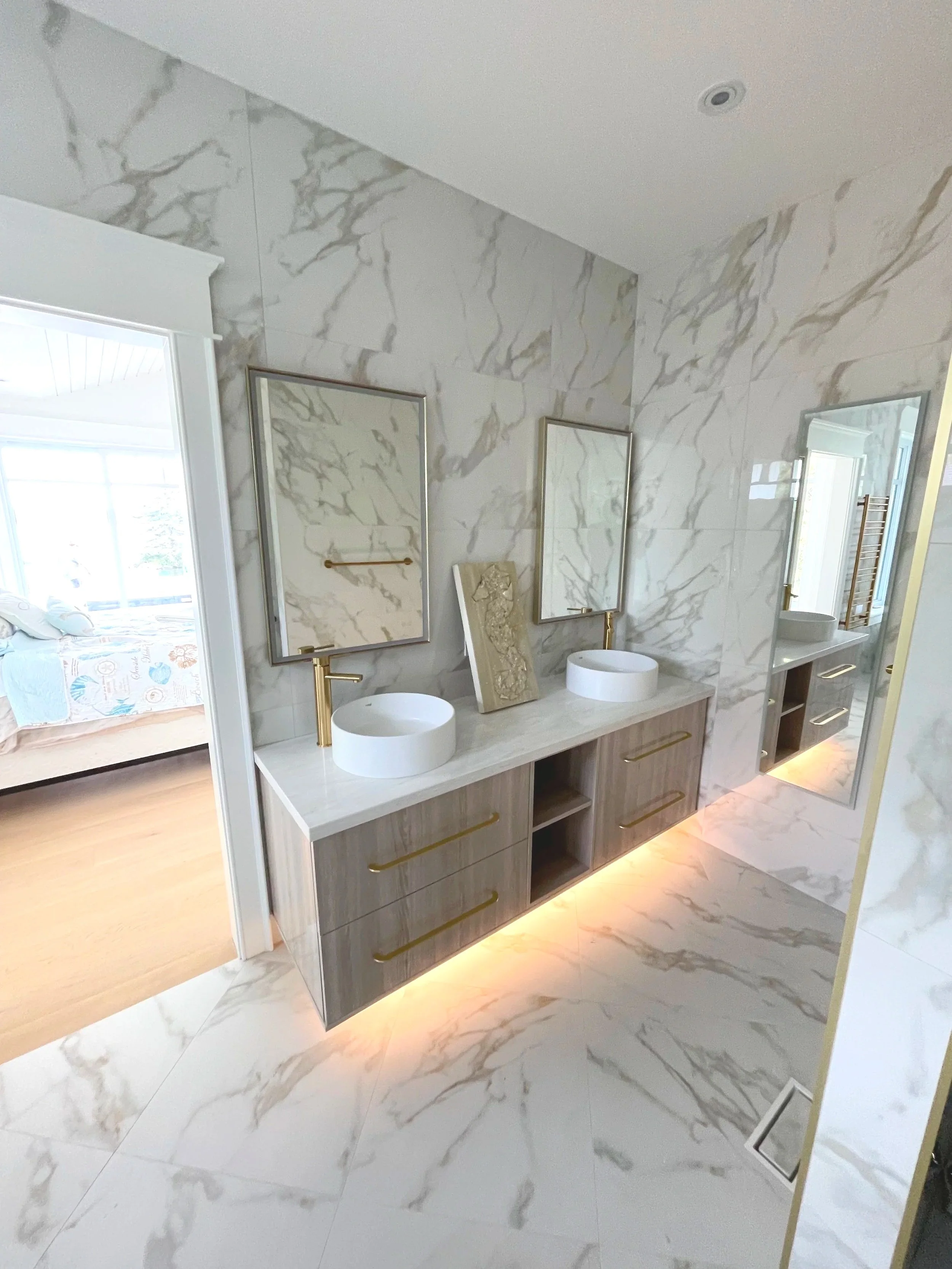 Modern bathroom with marble walls and floor, dual sinks on a wooden vanity, large mirrors, gold fixtures, and a full-length mirror.  Tile Work and Contractor Kawartha Lakes, GTA, Muskokas.