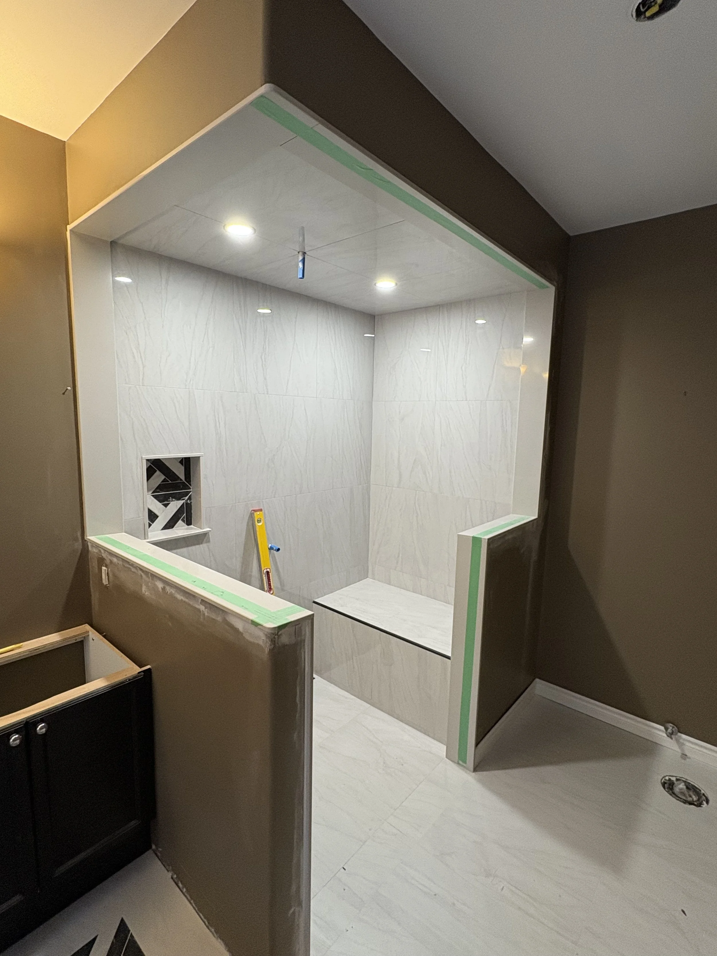Bathroom shower area under construction with marble walls, a built-in bench, recessed lighting. Green painter's tape outlines the edges.  Tile Work and Contractor Kawartha Lakes, GTA, Muskokas. Bathroom renovation