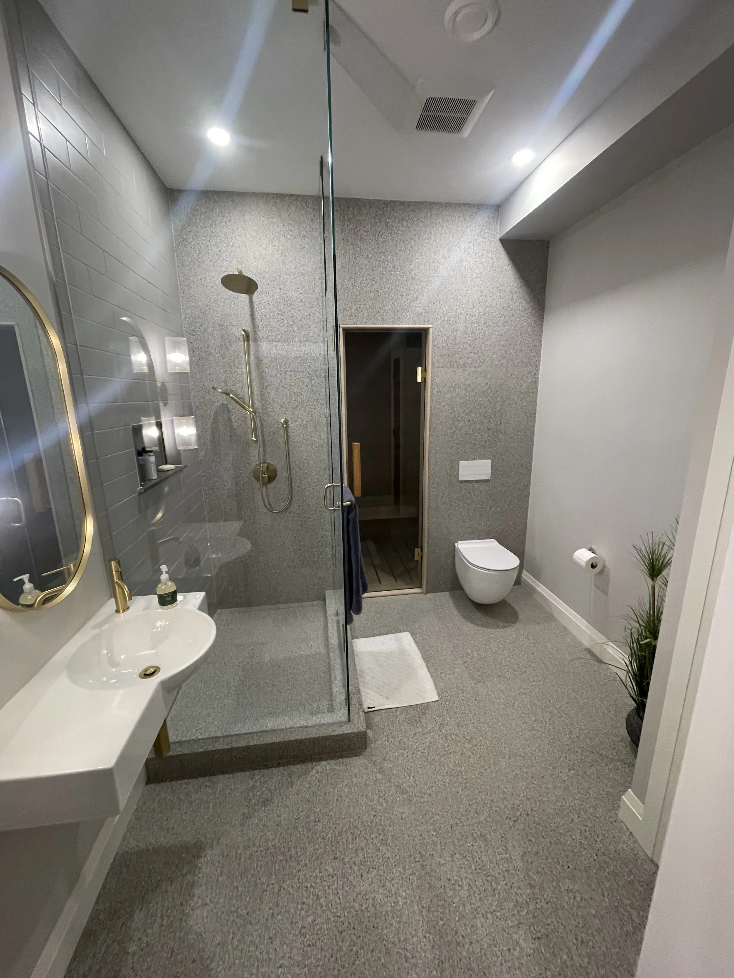 Modern bathroom with a walk-in shower, sleek grey tile work, a mounted rain shower head, and a handheld shower, a white wall-mounted sink with gold fixtures.  Tile Work and Contractor Kawartha Lakes, GTA, Muskokas.