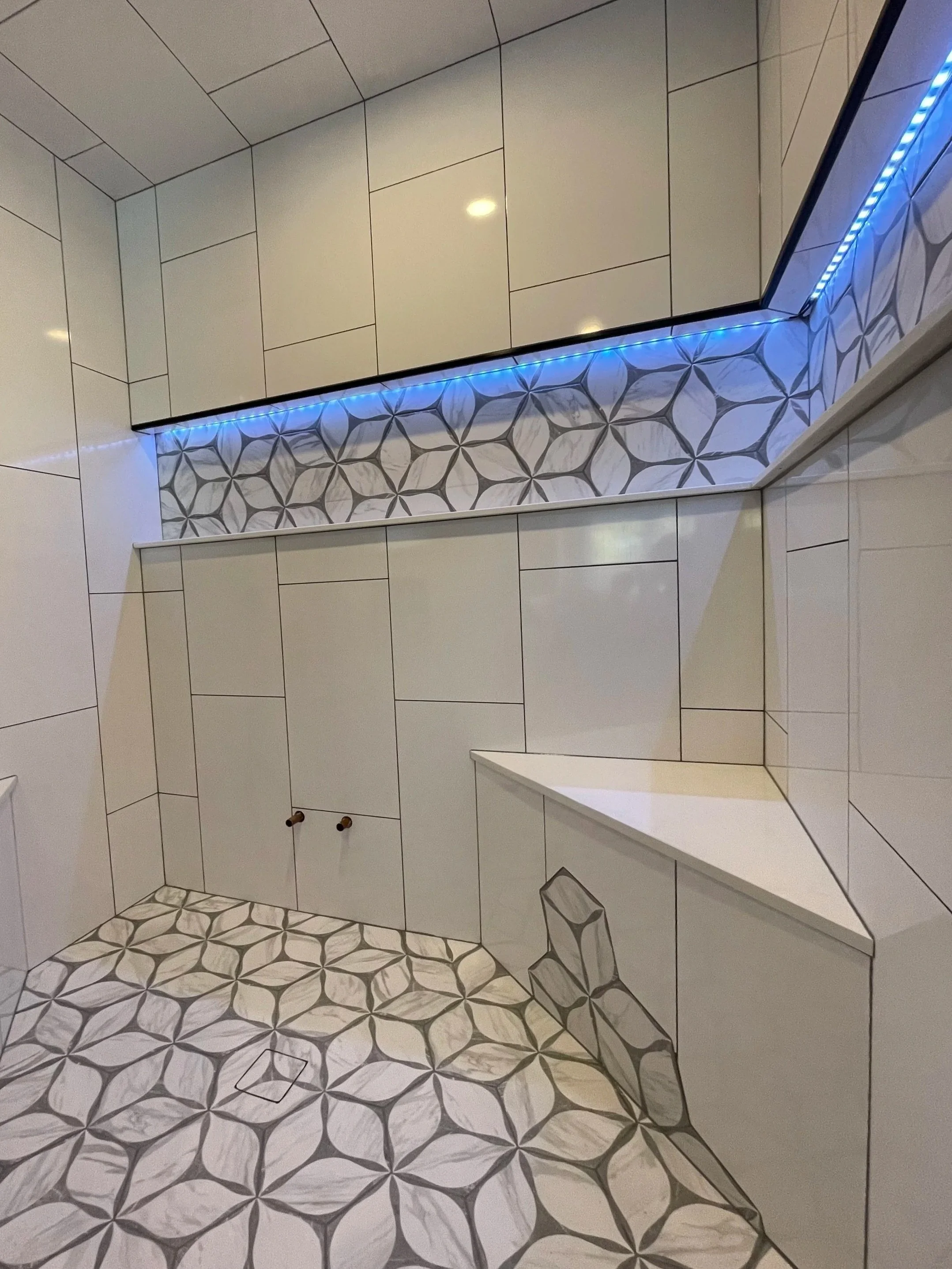 Modern bathroom with white tiled walls and geometric patterned floor and back wall tiles, blue LED lights backlighting the tile.  Tile Work and Contractor Kawartha Lakes, GTA, Muskokas.