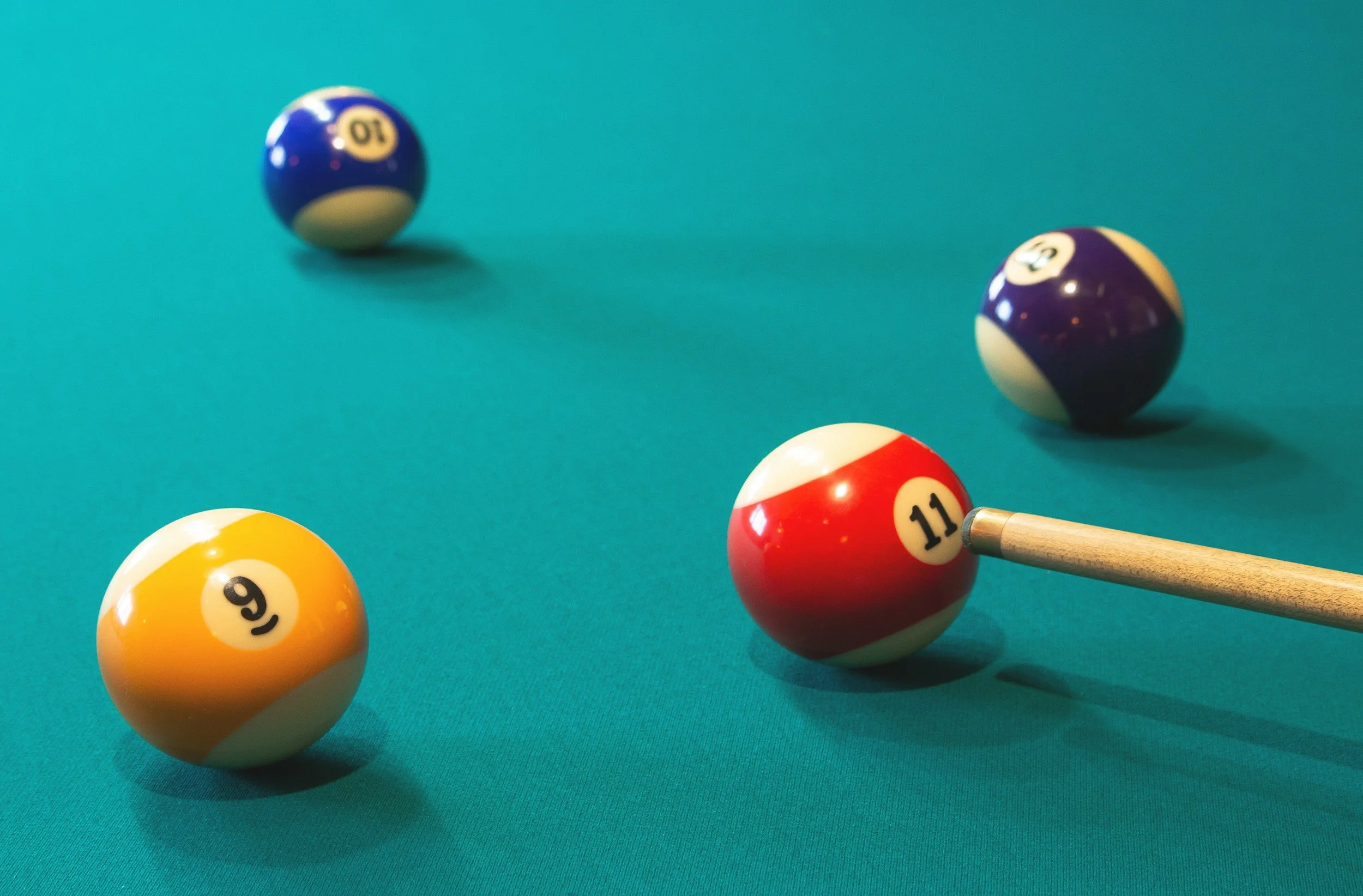 Billiard balls on a green pool table, with the 11-ball in position for shot, and the 9-ball, 10-ball, 12-ball, and 13-ball scattered in the background.