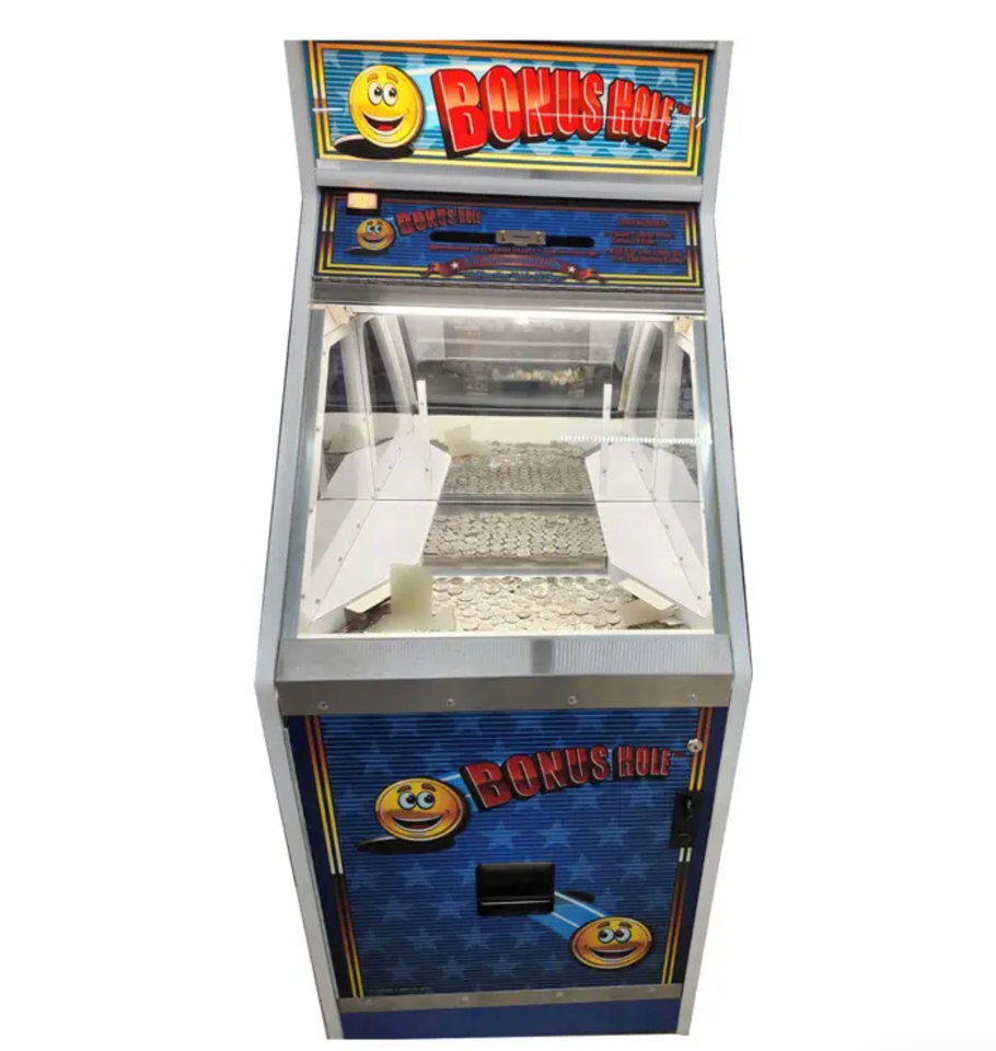 An empty coin pusher arcade game machine with a colorful sign that says 'Bonus Hole' and features a smiling emoji face.