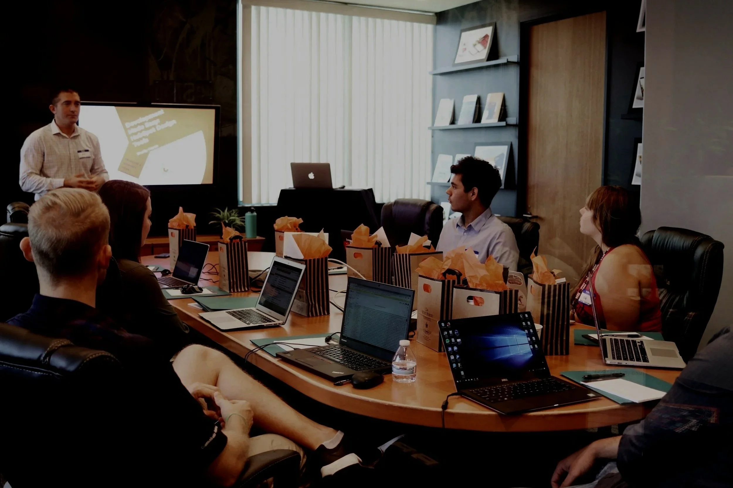 People attending a business presentation in a conference room with gift bags and laptops on the table.