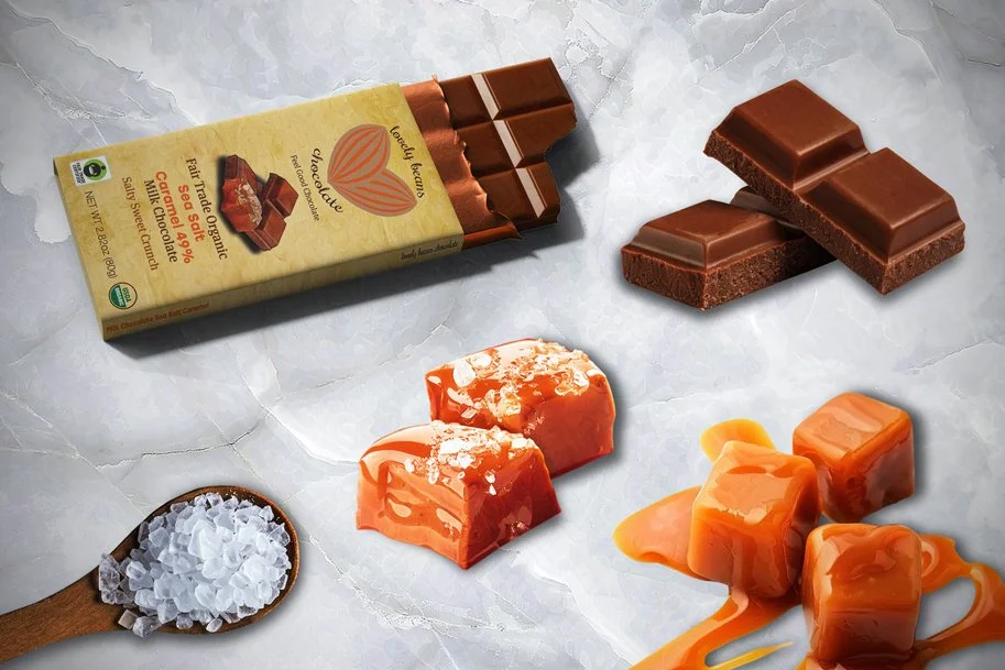 A milk chocolate bar and chocolate pieces, caramel candies, and sea salt on a marble background, showcasing delicious organic treats.