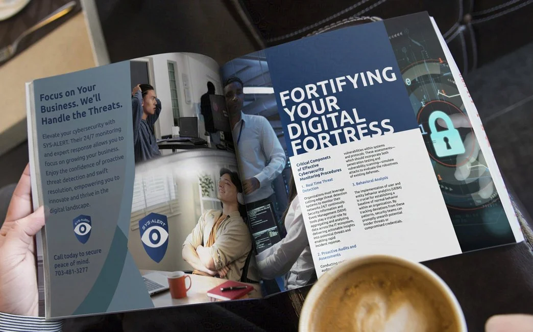 A person holds a magazine open to a cybersecurity-themed spread. The left page shows a SYS-ALERT ad "Focus on Your Business. We'll Handle the Threats." The right shows business professionals and security graphics.